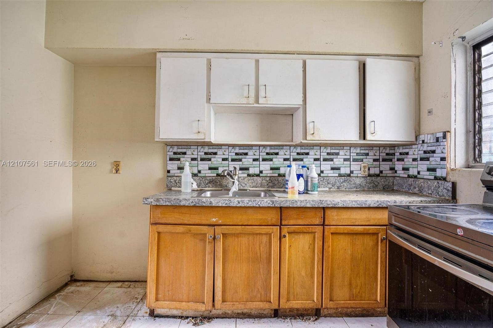 50 NW 69th Street, Miami, FL 33150 Kitchen featuring wooden lower cabinetry, white upper cabinets, stone-composite countertops, multi-toned decorative tile backsplash, and stainless steel dual-basin sink
