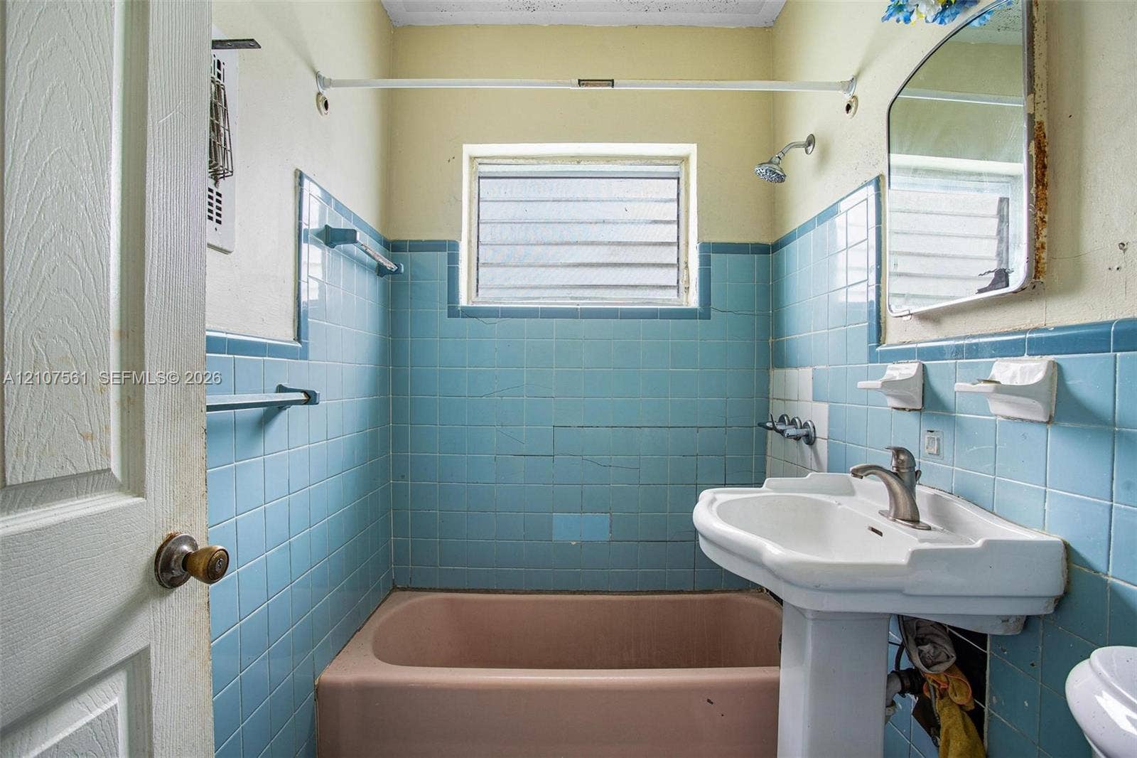 50 NW 69th Street, Miami, FL 33150 Bathroom featuring blue ceramic wall tiling, a porcelain pedestal sink with a metallic faucet, a built-in bathtub, and a window with jalousie glass panes