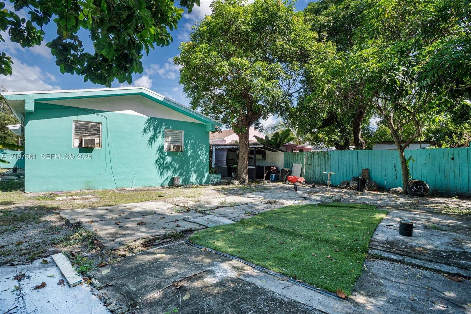 50 NW 69th Street, Miami, FL 33150 Exterior view featuring a concrete-block structure with a low-slope roof, expansive backyard, mature shade trees, and a tall painted wood fence