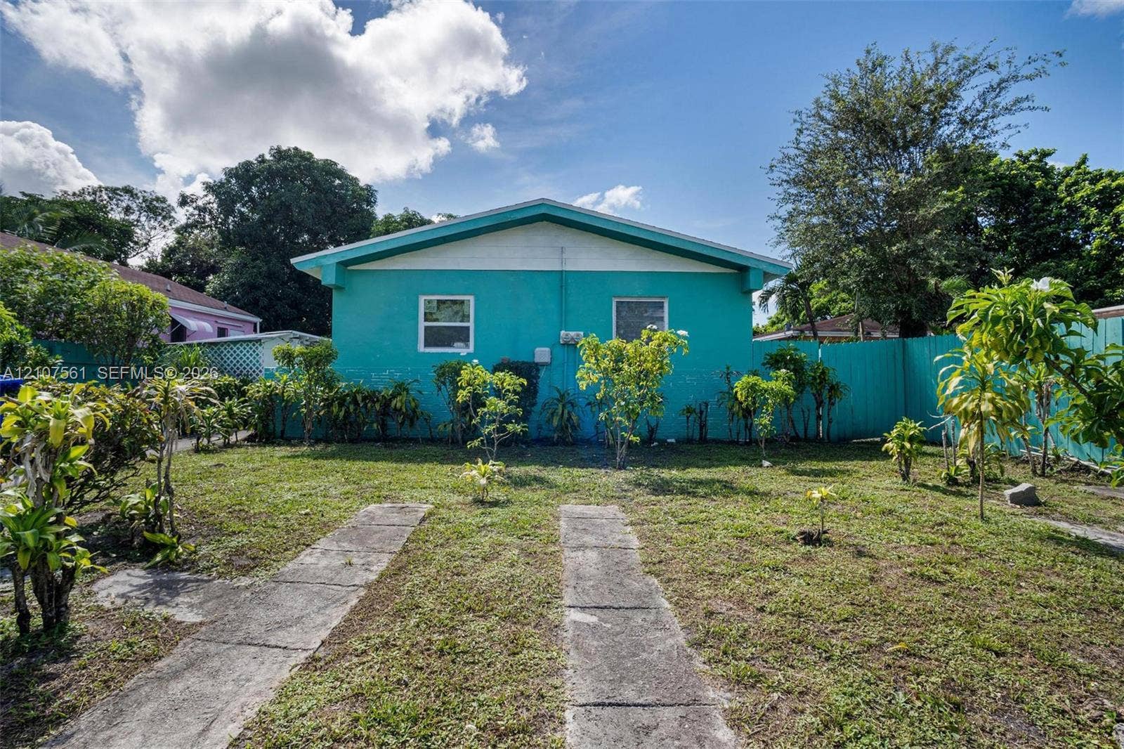 50 NW 69th Street, Miami, FL 33150 Exterior rear elevation featuring a concrete structure with a gabled roofline, dual paved tracks, and a perimeter privacy fence