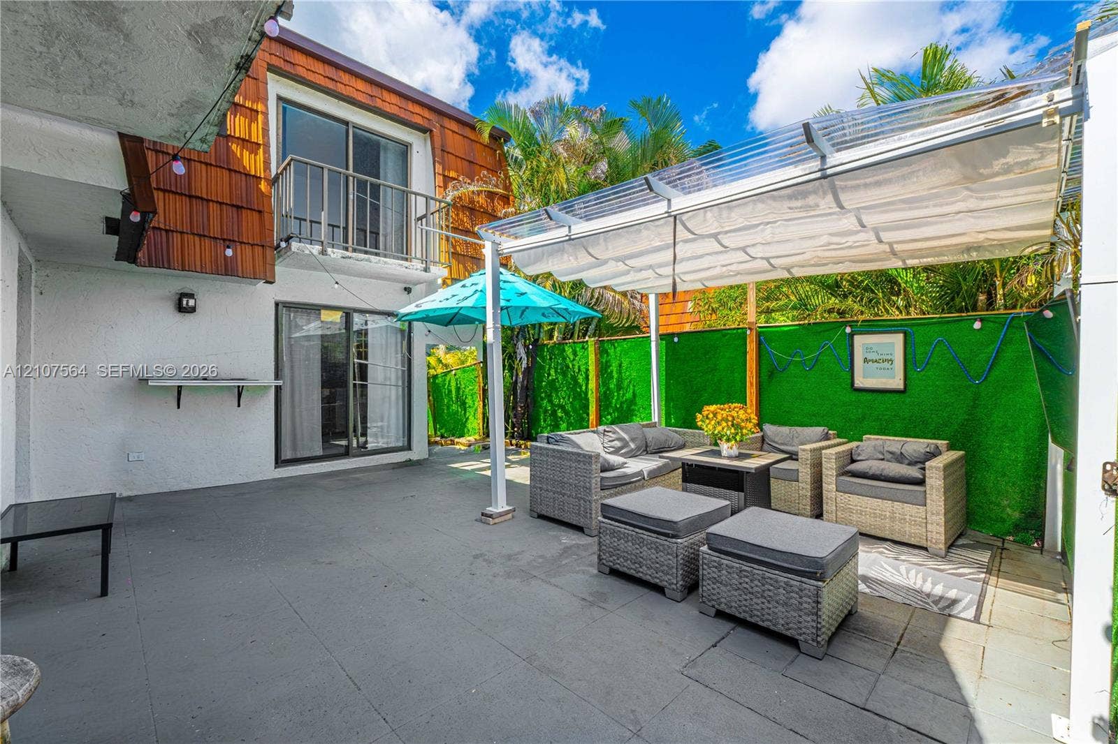 Paved ground-level patio featuring a retractable canopy cover, wood-shingle exterior siding, and second-level balcony with metal railing