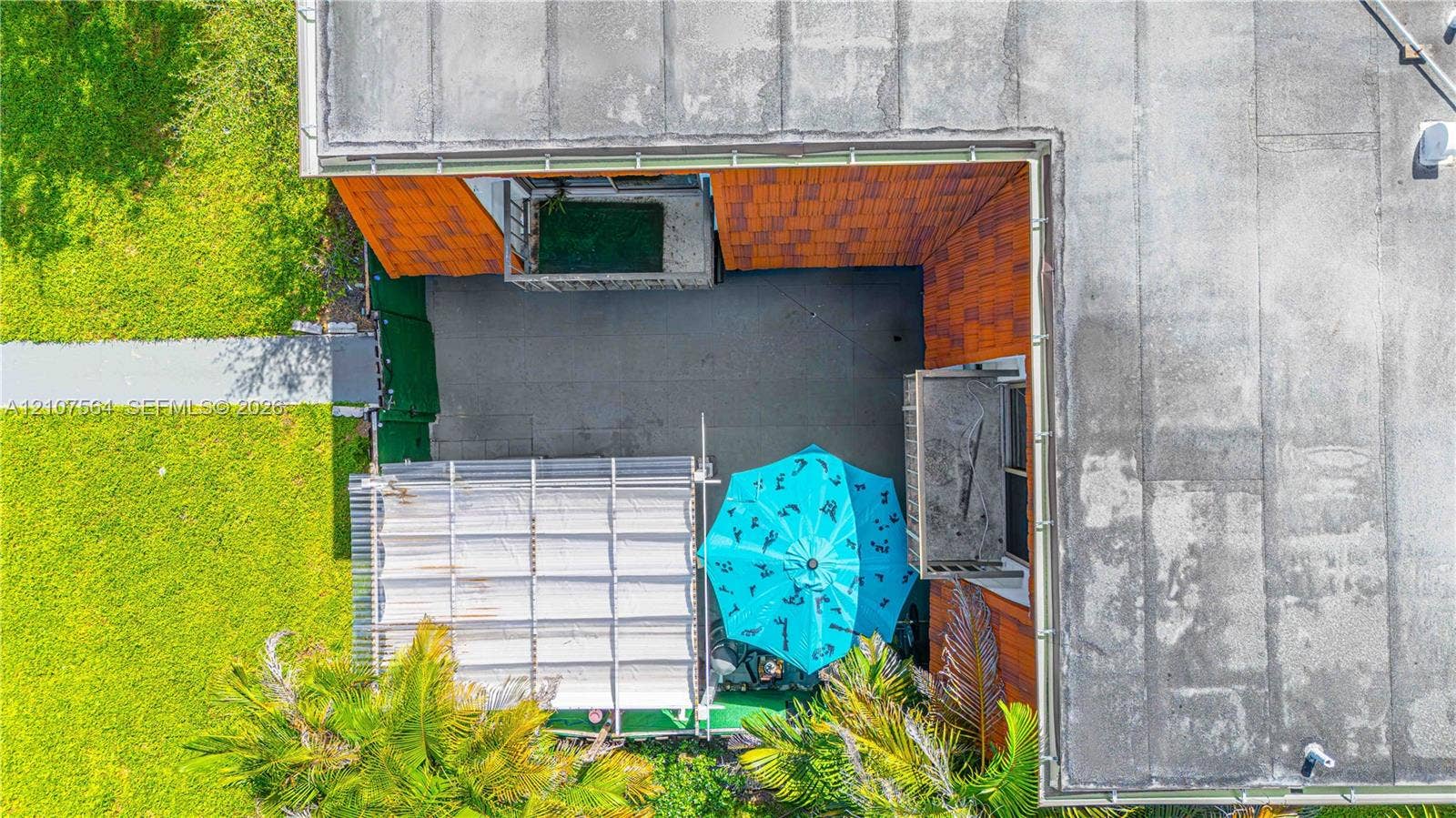 Aerial perspective of a courtyard featuring a flat roof structure, orange tiled exterior walls, concrete surfacing, and a corrugated metal patio cover