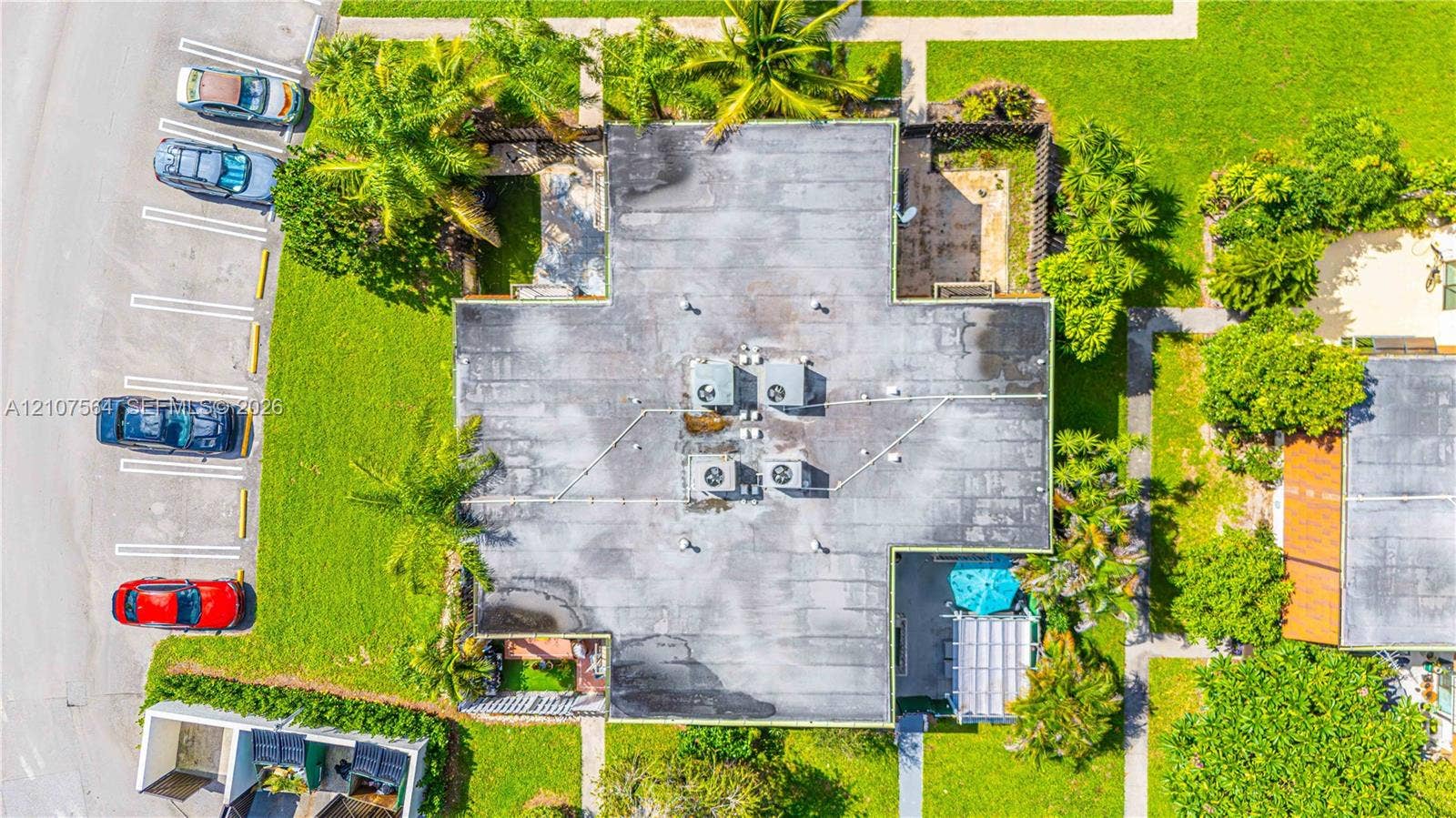 Aerial perspective of a property featuring dedicated parking spaces, mature palm trees, manicured lawns, and ground-level patios