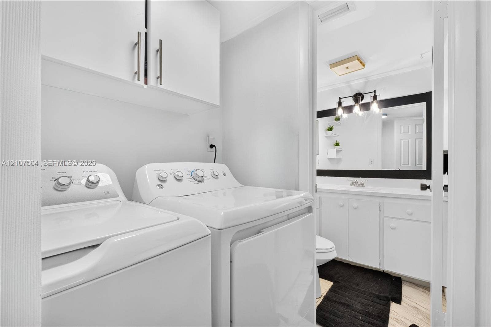 Laundry area featuring upper storage cabinetry and white cabinetry in the bathroom vanity with a framed mirror and three-light wall-mounted fixture
