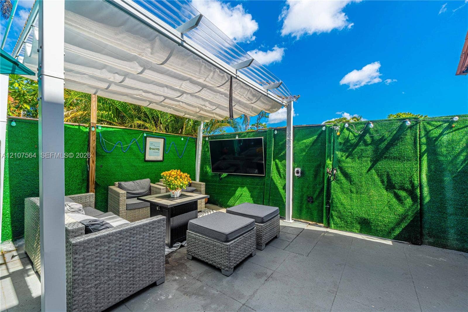 Outdoor patio featuring concrete tile flooring, a metal pergola with a retractable fabric canopy, and mounted wall-integrated artificial greenery privacy screens