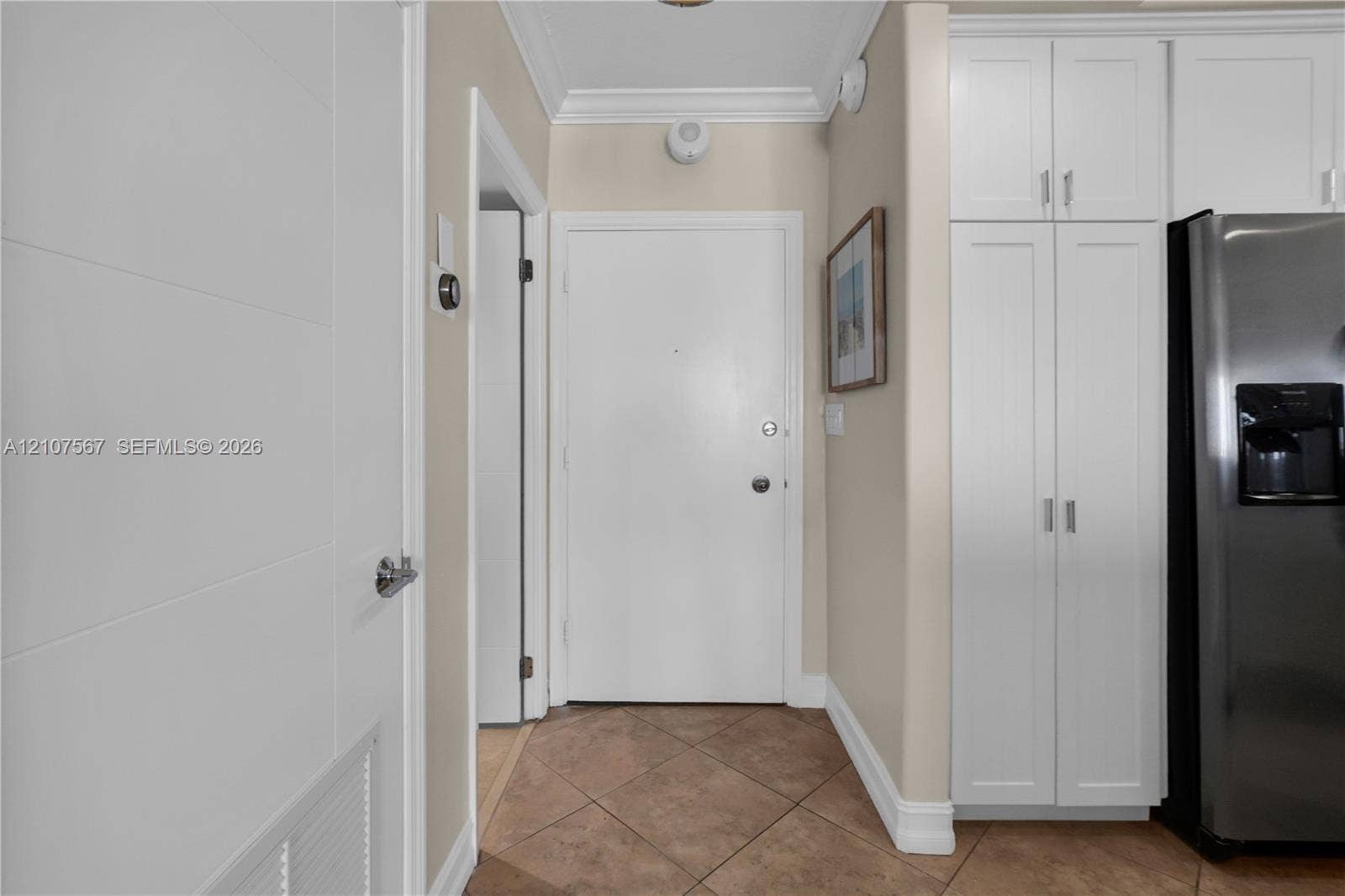 Entryway featuring tile flooring, crown molding, floor-to-ceiling white cabinetry with silver hardware, and a solid-core door