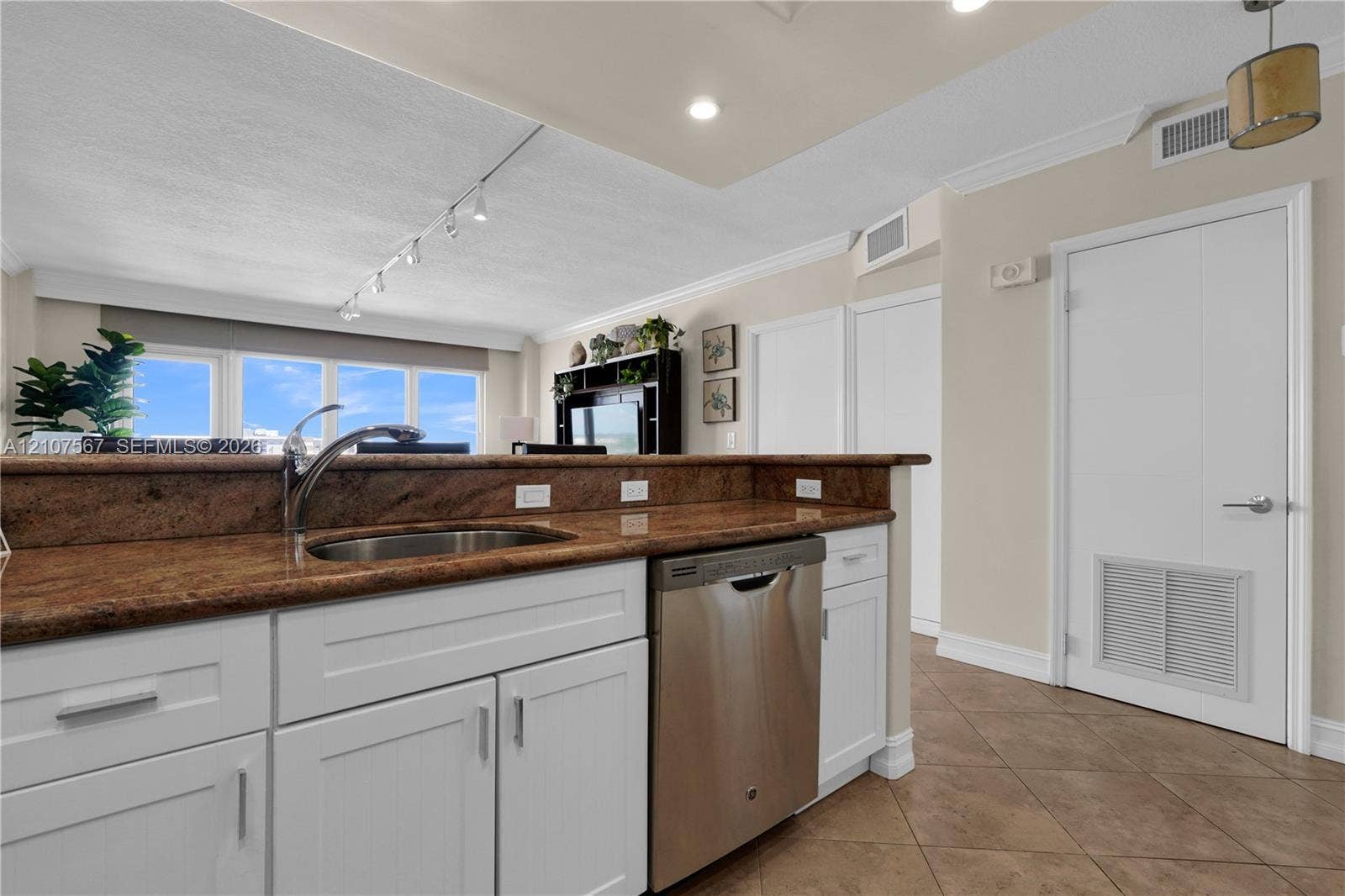 Kitchen featuring white shaker-style cabinetry, stone-surface countertops, an undermount stainless steel sink, a stainless steel dishwasher, and tile flooring