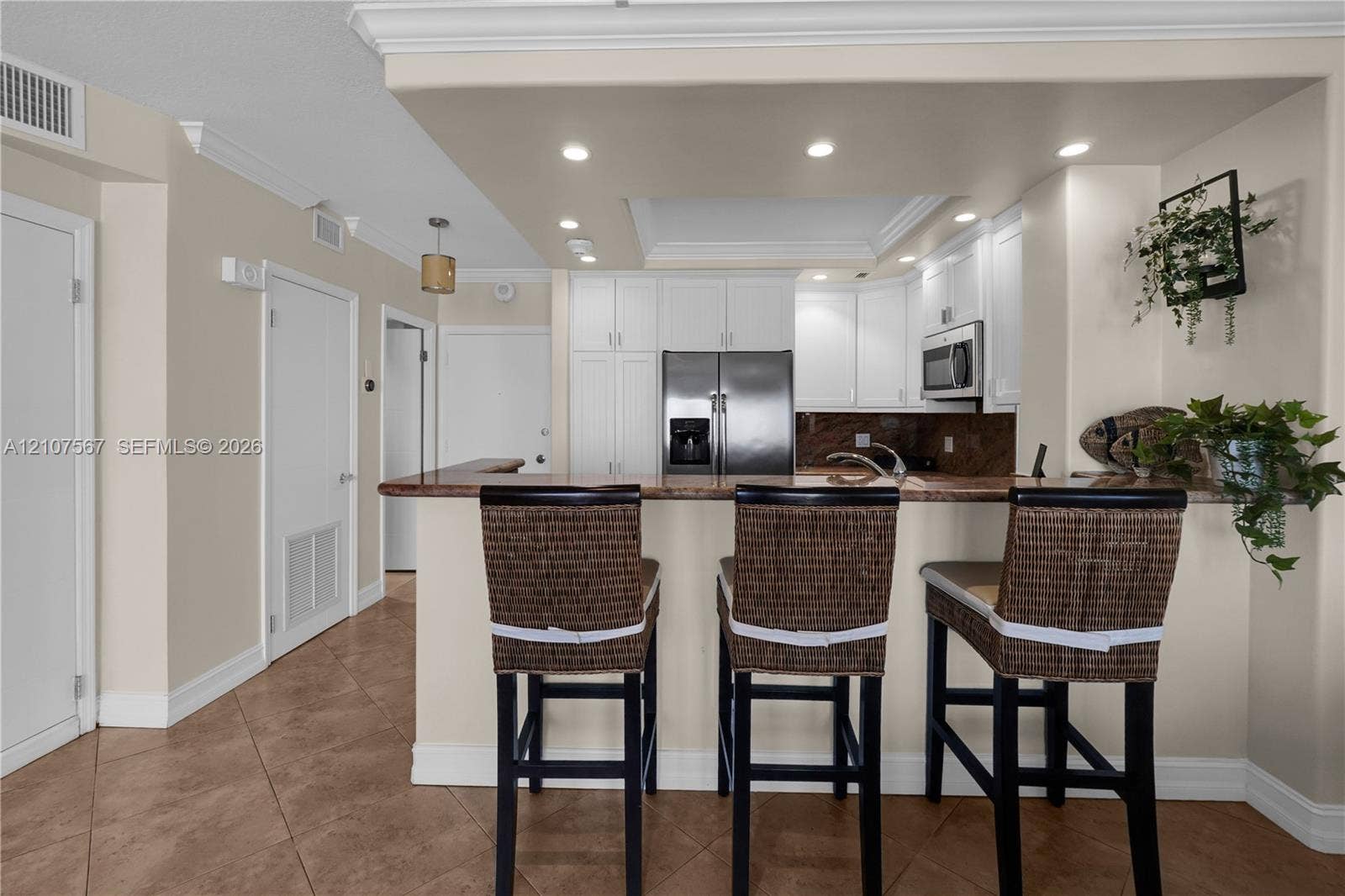 Kitchen featuring white shaker-style cabinetry, stone countertops, stainless steel appliances, breakfast bar, and recessed lighting