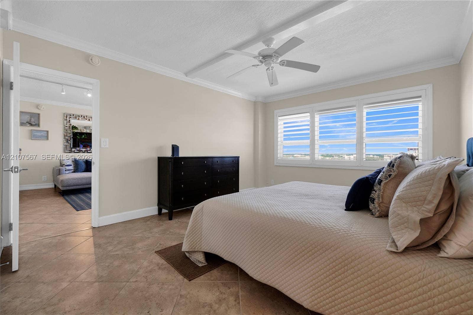 Neutral-toned walls, tile flooring, crown molding, white-finish ceiling fan, and large windows with horizontal blinds