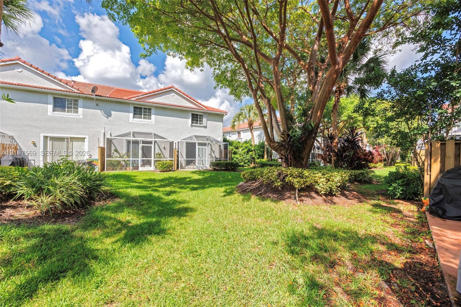 3765 San Simeon Circle, #3765, Weston, Weston, FL 33331 Rear exterior featuring a multi-level stucco facade, red tile roofing, multiple screened-in porches, and a mature tree within a landscaped lawn