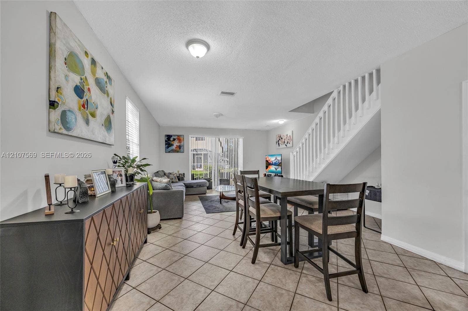 3765 San Simeon Circle, #3765, Weston, Weston, FL 33331 Neutral-toned interior space featuring diagonal-set tile flooring, white-painted staircase with matching balusters, and glass sliding doors providing exterior access