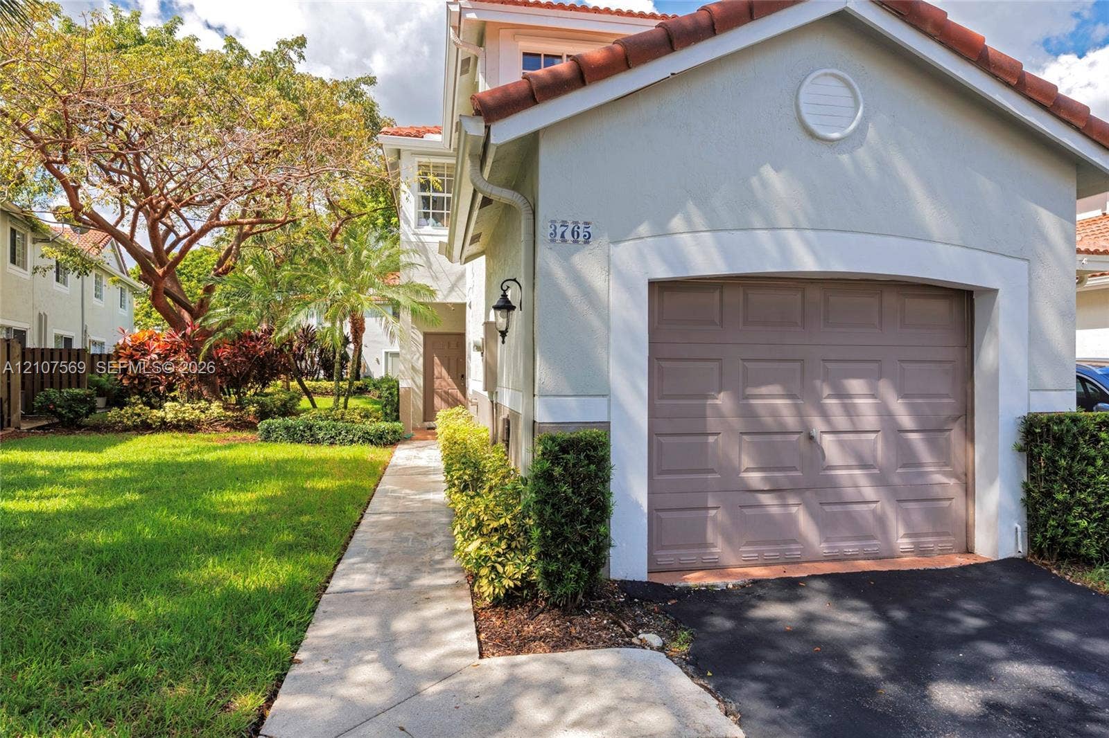 3765 San Simeon Circle, #3765, Weston, Weston, FL 33331 Exterior facade featuring stucco siding, a tiled roof, a single-car garage, and a concrete walkway bordered by manicured landscaping
