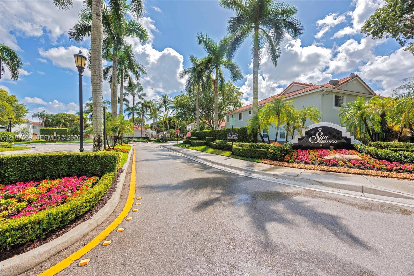 3765 San Simeon Circle, #3765, Weston, Weston, FL 33331 Paved entryway featuring mature palm trees, manicured hedges, colorful floral landscaping, and dedicated post-mounted street lighting
