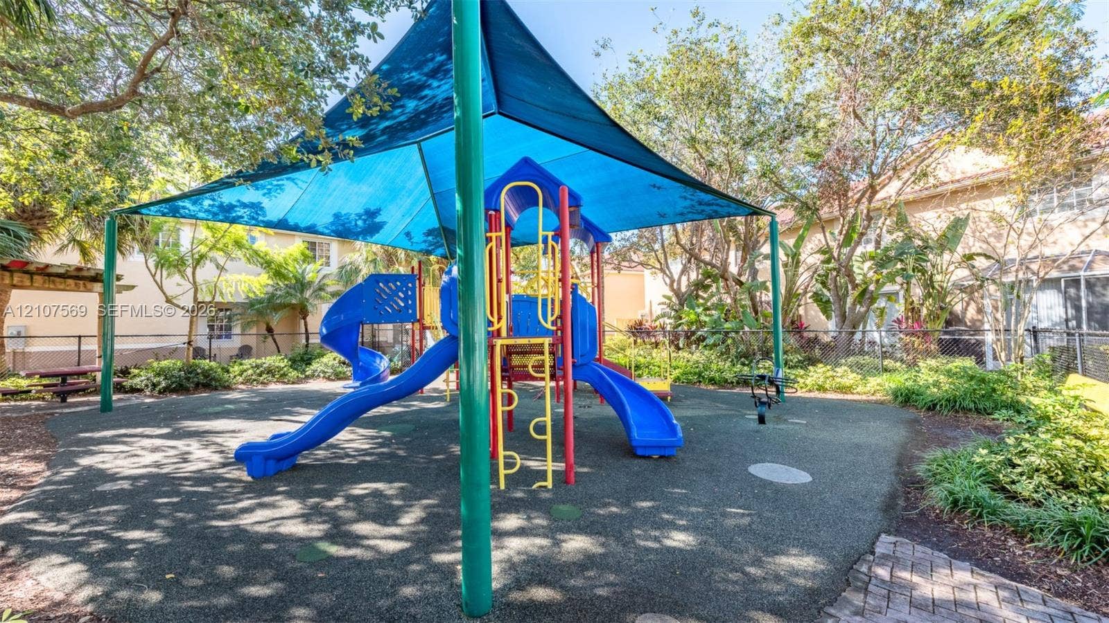 3765 San Simeon Circle, #3765, Weston, Weston, FL 33331 Playground featuring a central climbing structure with dual slides, a fabric shade canopy, rubberized flooring, and surrounding landscaping