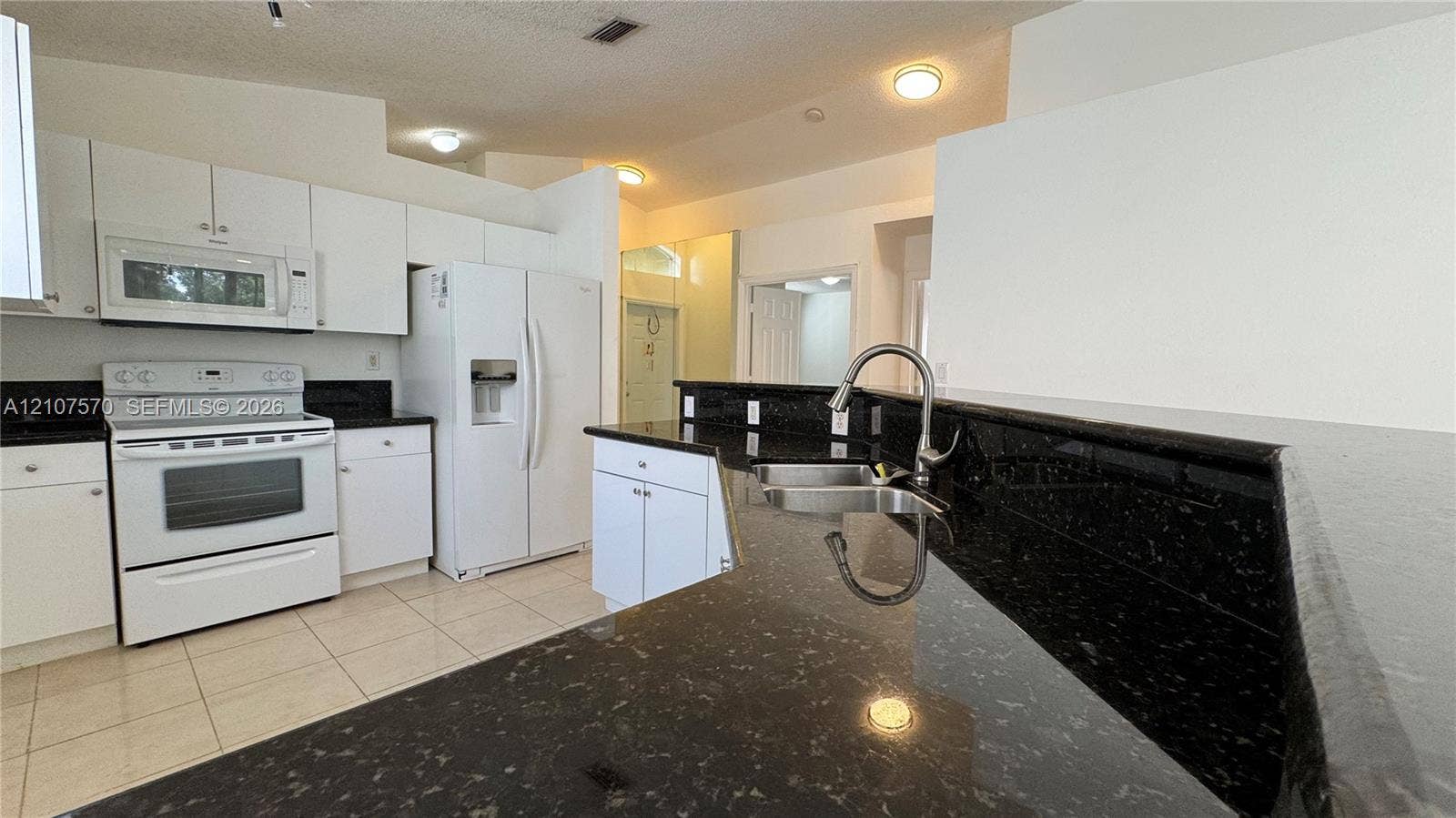 Kitchen featuring white cabinetry, dark stone countertops, tile flooring, built-in white appliances, and a stainless steel kitchen faucet