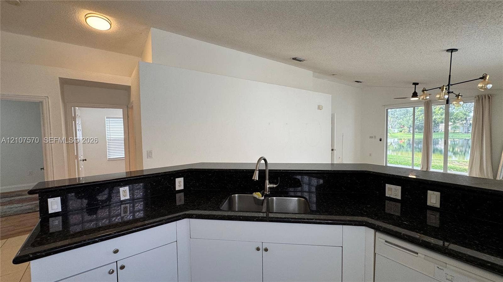 Kitchen featuring a wraparound dark stone countertop, double-basin undermount sink with a gooseneck faucet, white cabinetry, and a multi-arm chandelier