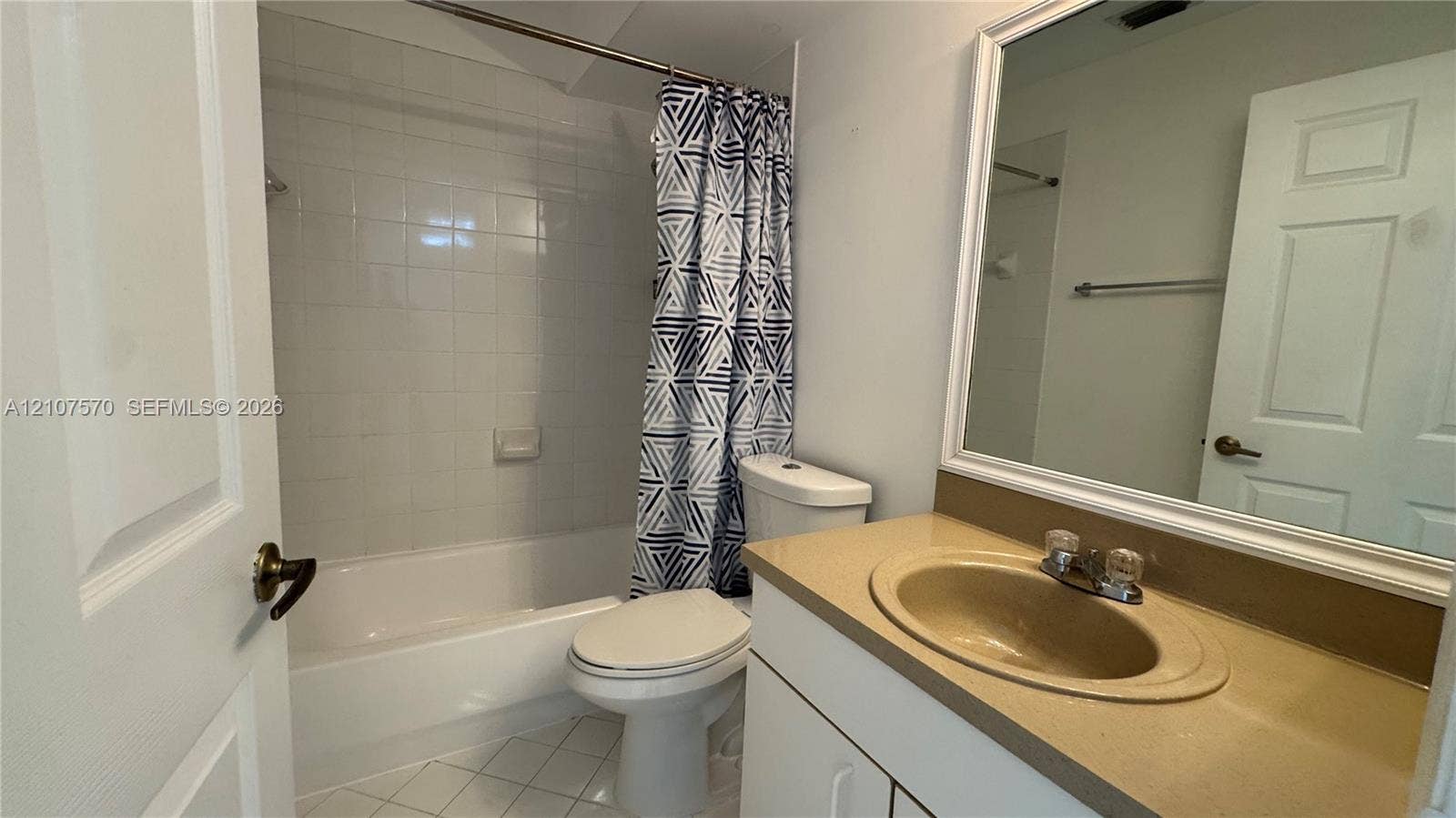 Bathroom featuring a vanity with a solid-surface integrated sink, a full-width mirror, tile flooring, and a shower-tub combination with a tiled surround