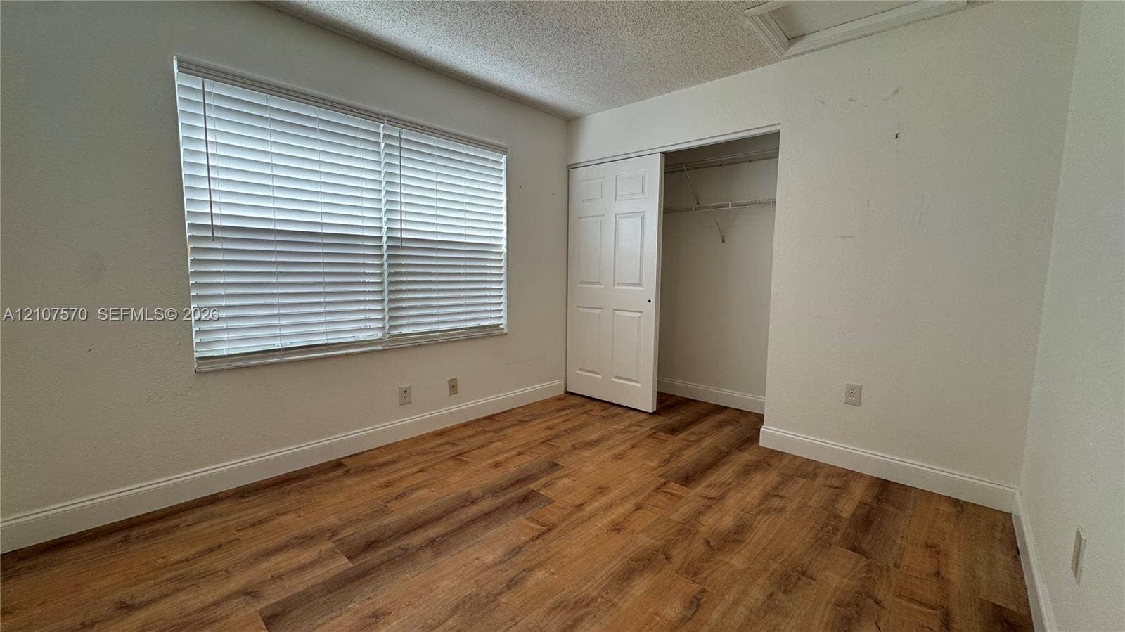 Wood-finish flooring, white walls, horizontal window blinds, and a closet with a six-panel door