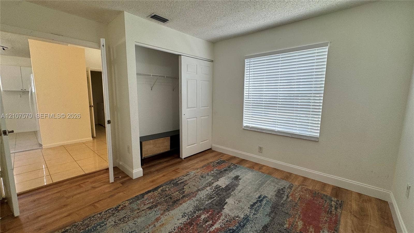 Wood-finish flooring, sliding door closet with built-in shelving, and window with installed horizontal blinds