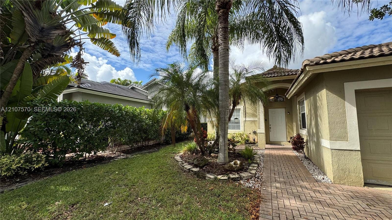 Exterior facade featuring a stucco finish, arched entryway, brick-paver walkway, tile roof, and mature palm landscaping