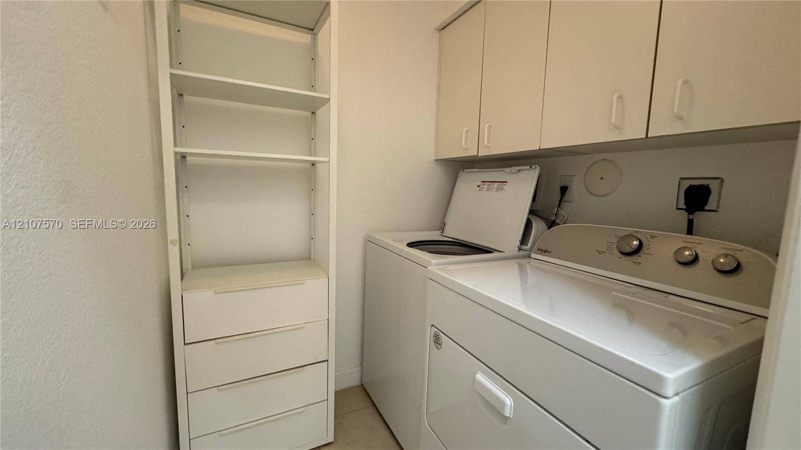 Laundry area featuring built-in floor-to-ceiling shelving with integrated storage drawers and wall-mounted upper cabinetry