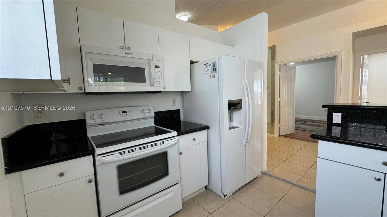 Kitchen featuring white cabinetry, dark stone countertops, white appliances, and tile flooring