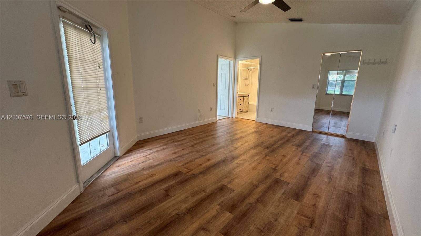 Interior space featuring wood-finish flooring, vaulted ceilings with a mounted fan, a glass-panel door with integrated blinds, and mirrored sliding closet doors