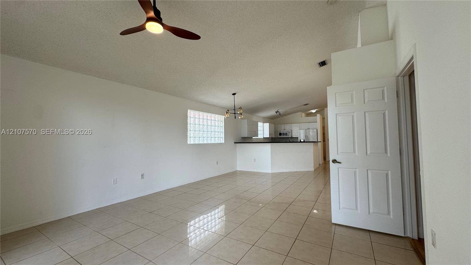 Open-concept interior featuring large-format tile flooring, vaulted ceilings, a structural glass block window, and a ceiling fan with integrated lighting