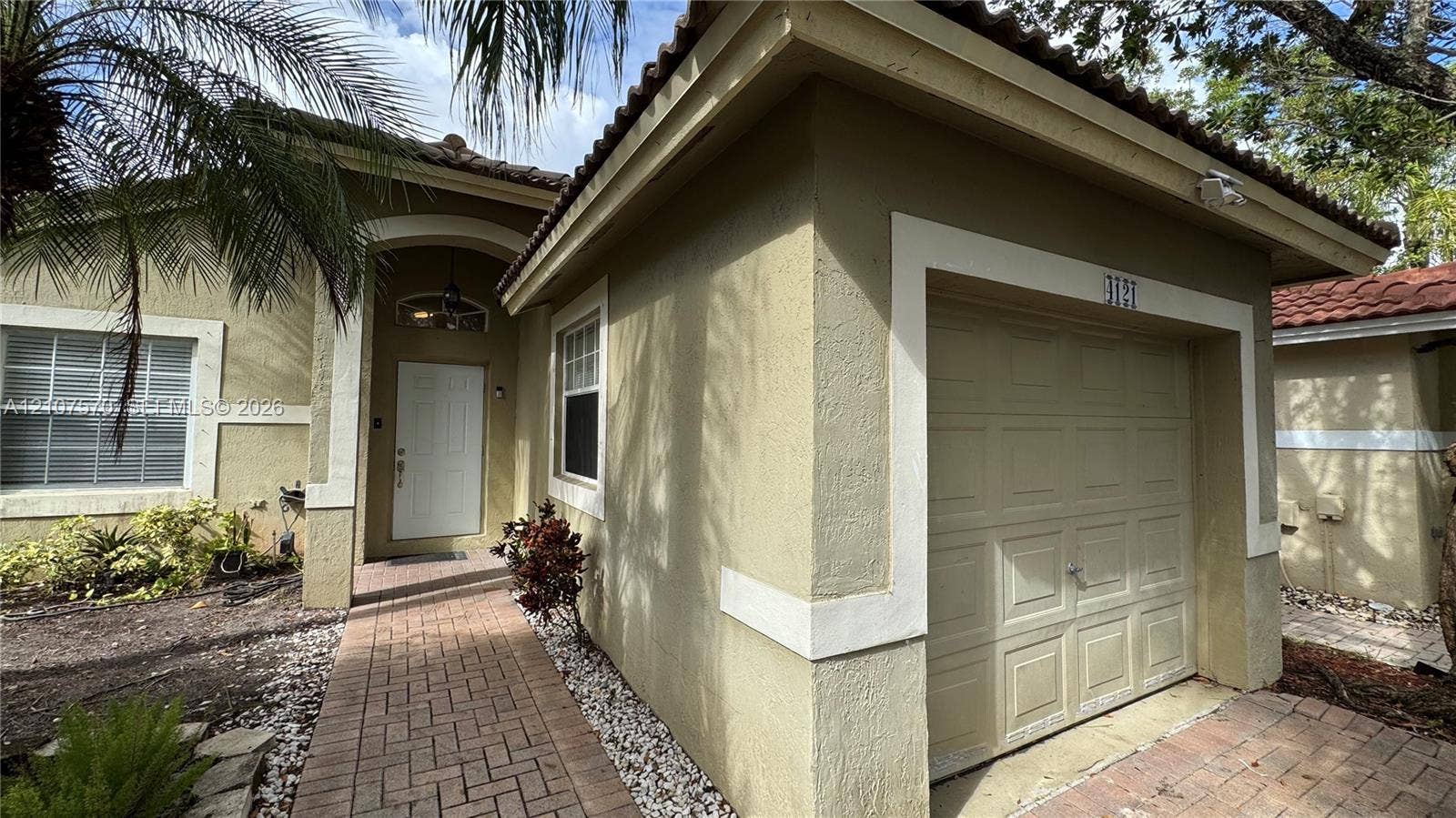 Stucco exterior with decorative trim, tile roof, arched entryway, brick-paver walkway, and single-car garage