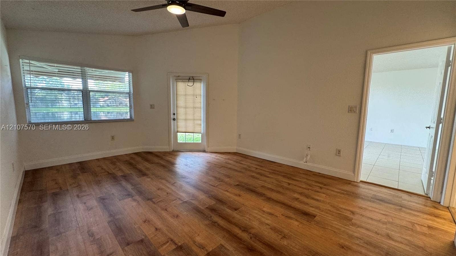 Vaulted ceiling with a central integrated light fixture and ceiling fan, wood-finish flooring, and natural light from a dual-pane window and a glass-paneled door