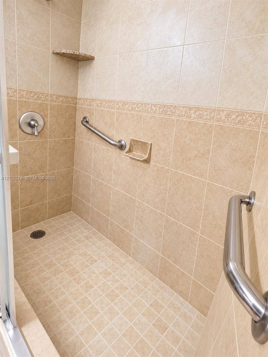 1425 Atlantic Shores Boulevard, #501, Hallandale Beach, FL 33009 Walk-in shower featuring ceramic wall and floor tiling, decorative accent border, built-in corner shelf, and stainless steel grab bars