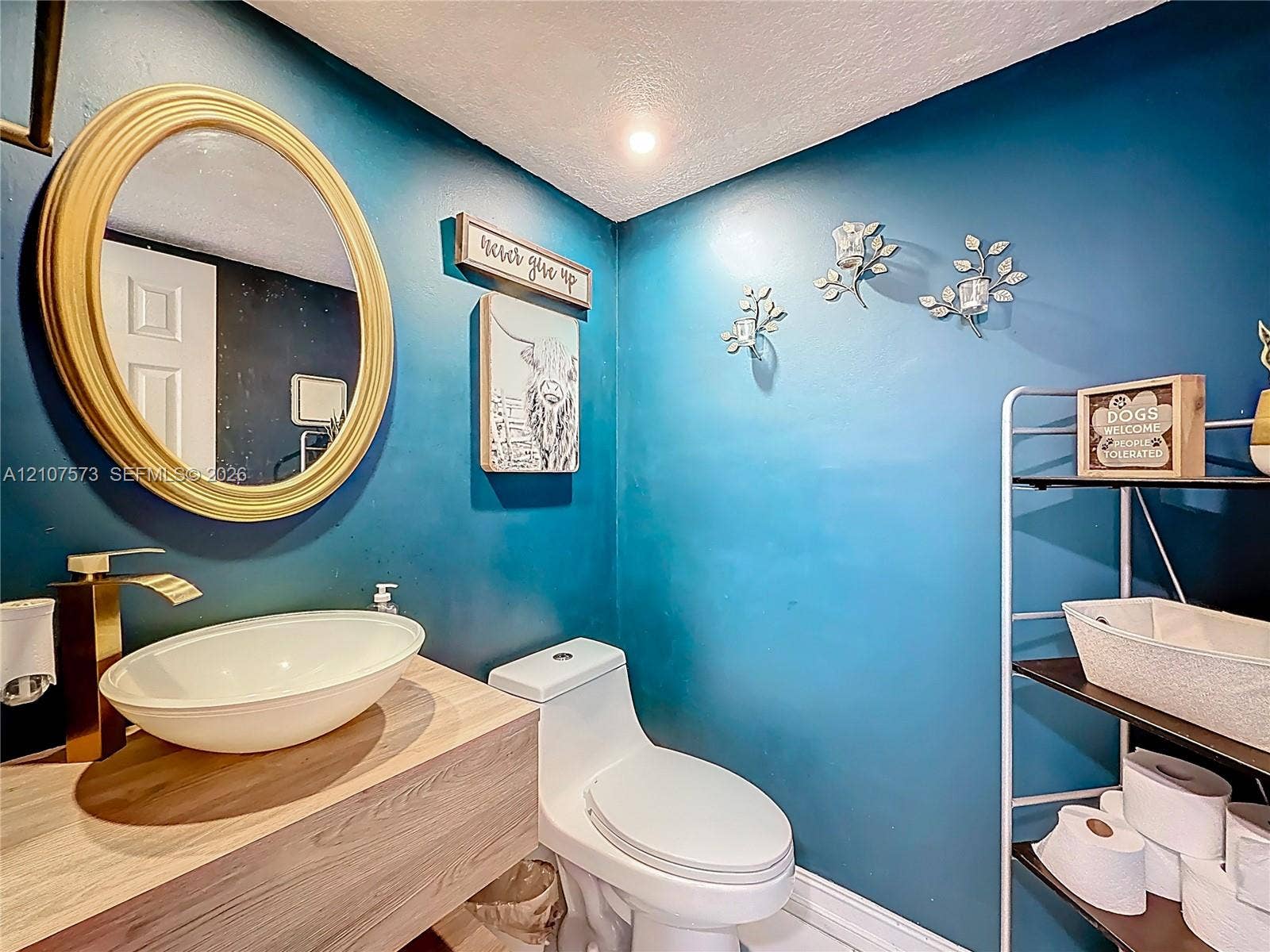 1291 SW 124th Court, #19-B, Miami, FL 33184 Floating wood-finish vanity with an oval vessel sink and metallic finish faucet, accompanied by an oval-framed wall mirror and wall-mounted light fixtures