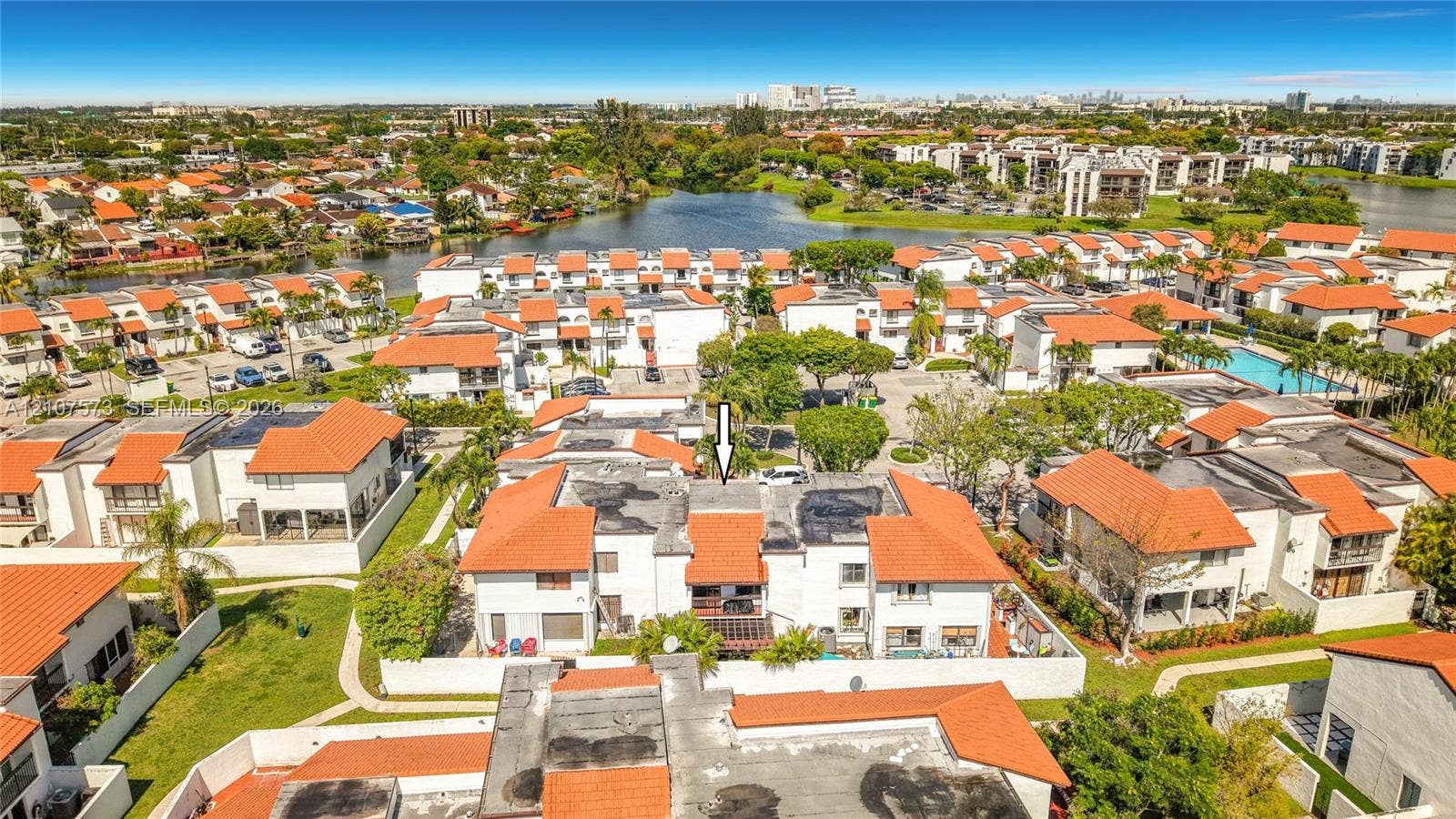 1291 SW 124th Court, #19-B, Miami, FL 33184 Aerial perspective of a multi-level residential structure featuring a red tile roof, white stucco exterior, and ground-level enclosed patio space, situated within a community landscape