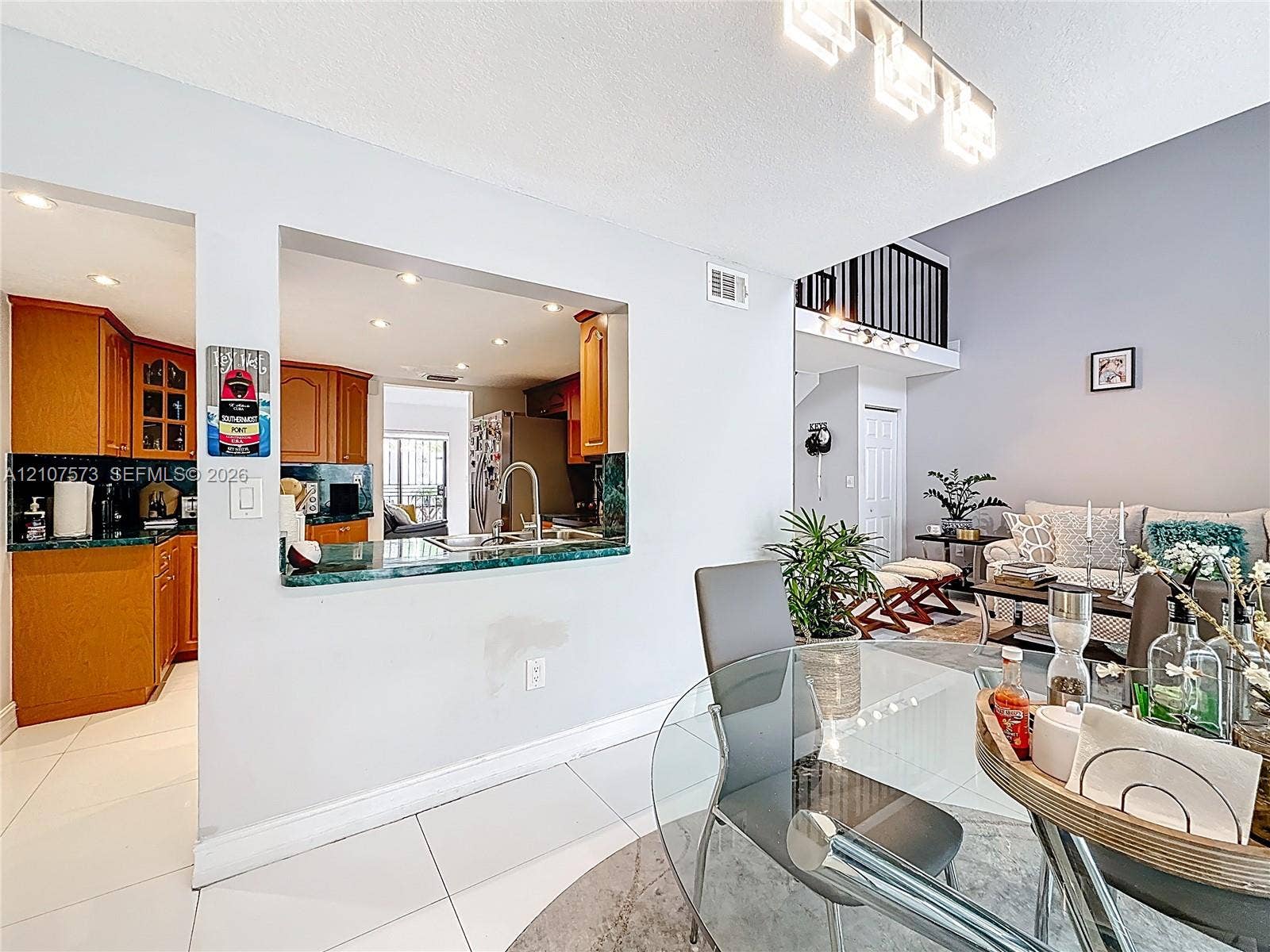 1291 SW 124th Court, #19-B, Miami, FL 33184 Kitchen features a pass-through window with a stone-surface countertop, cabinetry with glass-panel detailing, recessed lighting, and white tile flooring