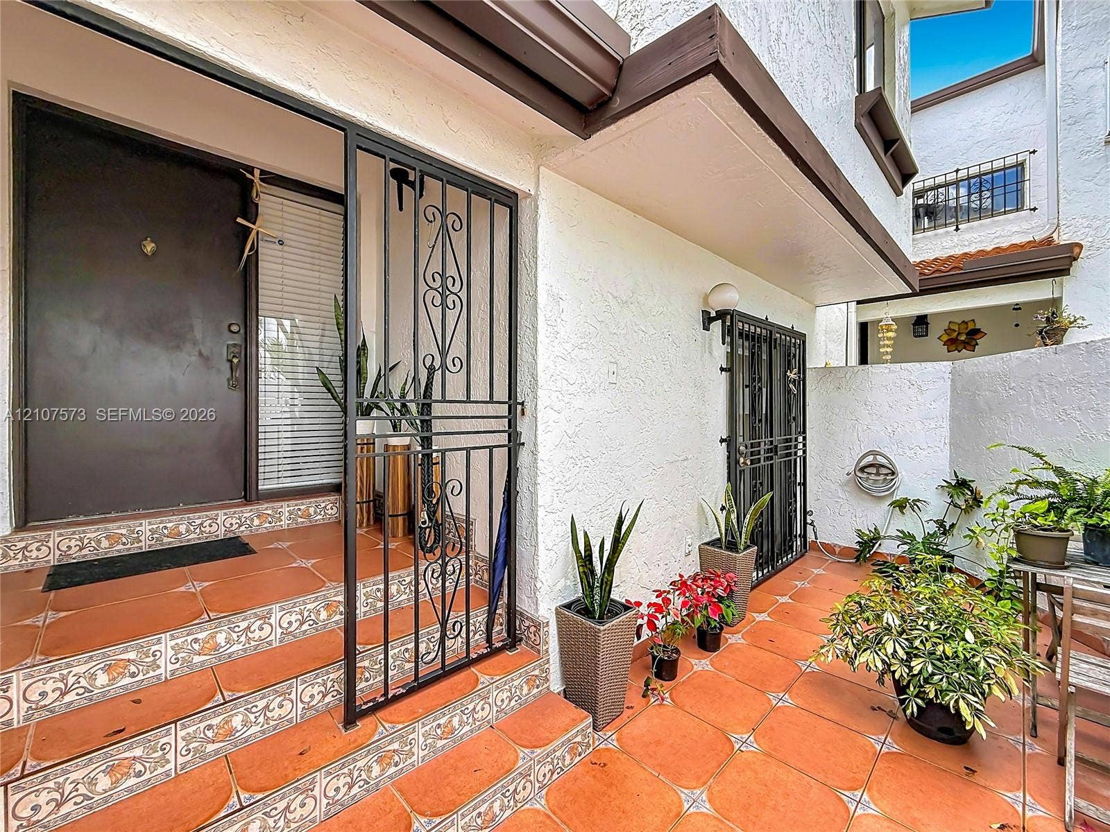 1291 SW 124th Court, #19-B, Miami, FL 33184 Private entryway featuring a decorative wrought iron security gate, textured exterior finish, and terracotta-style tile flooring with patterned accents