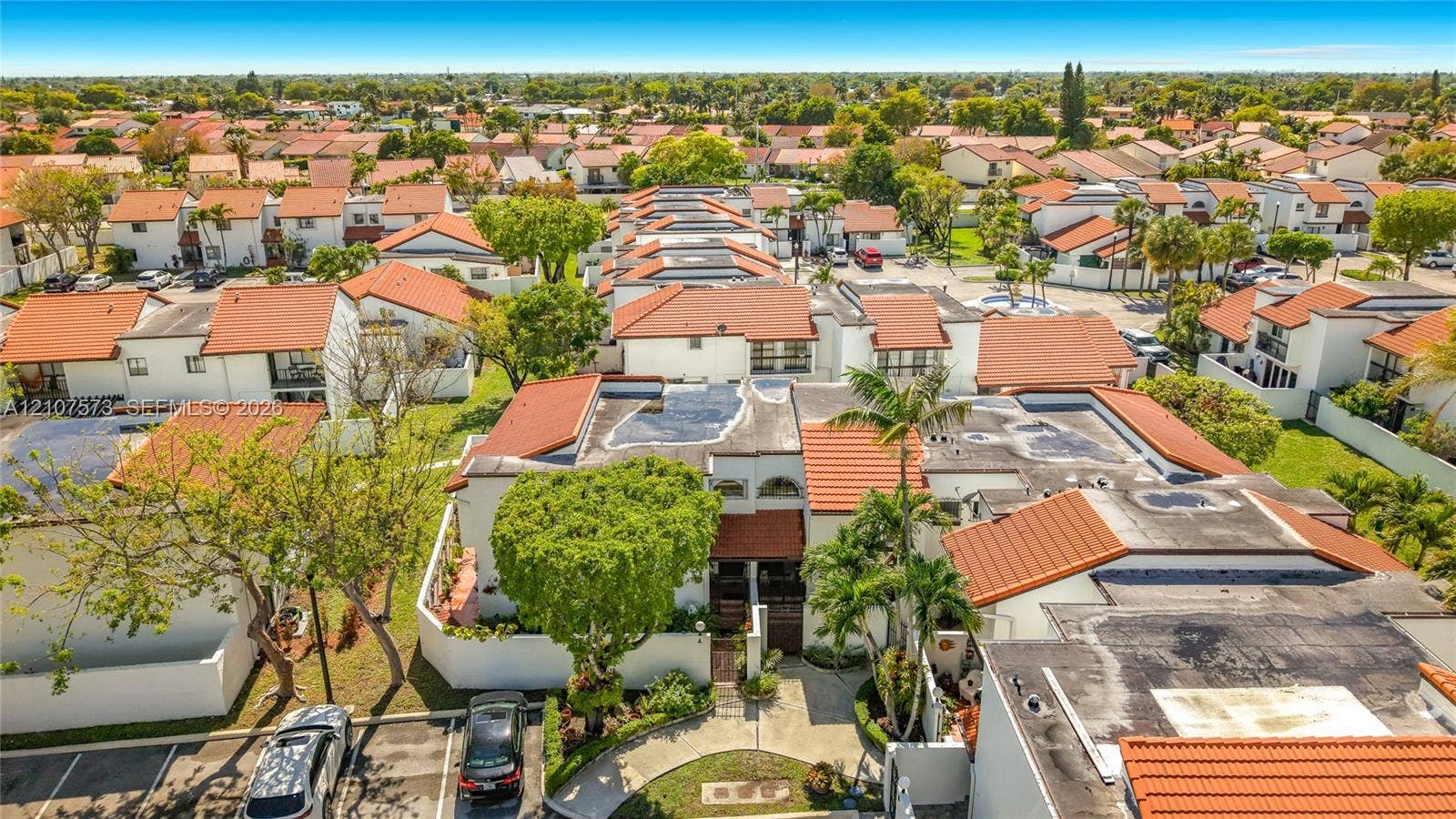 1291 SW 124th Court, #19-B, Miami, FL 33184 Aerial perspective featuring Spanish-style tile roofing, stucco exterior finishes, mature palm trees, and designated surface parking