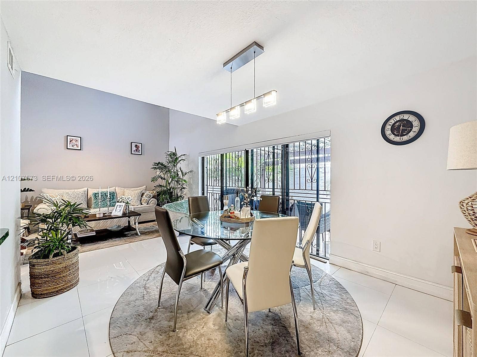 1291 SW 124th Court, #19-B, Miami, FL 33184 High-ceiling dining area featuring large-format tile flooring, a contemporary four-light linear pendant fixture, and sliding glass doors with metal security screening
