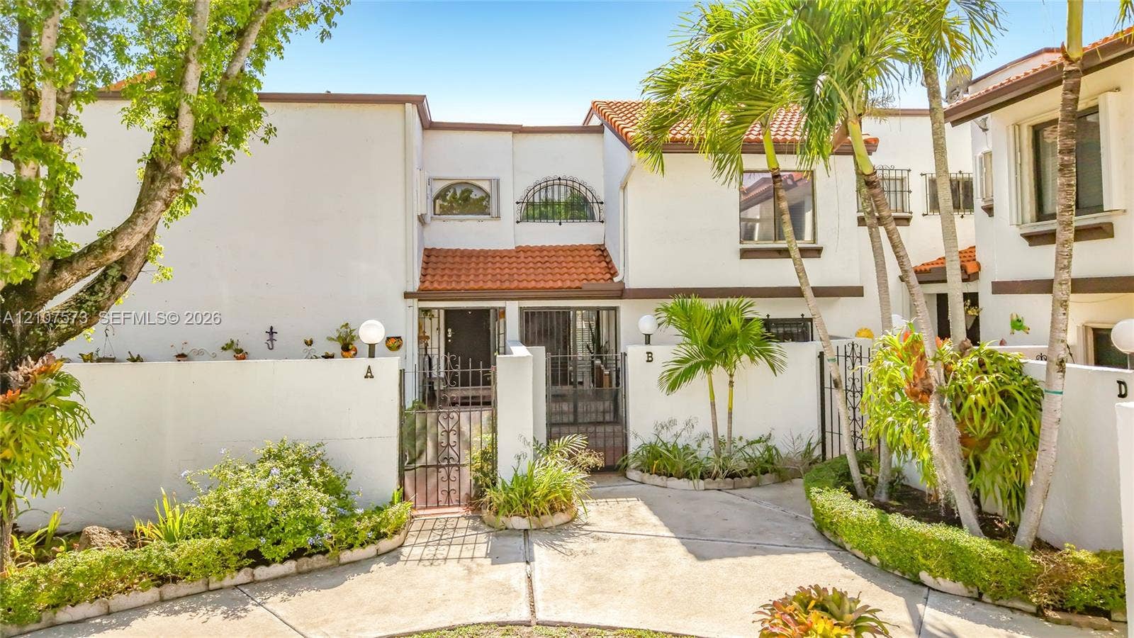 1291 SW 124th Court, #19-B, Miami, FL 33184 Stucco exterior featuring arched windows, tile roofing, decorative wrought-iron entry gates, and mature palm landscaping
