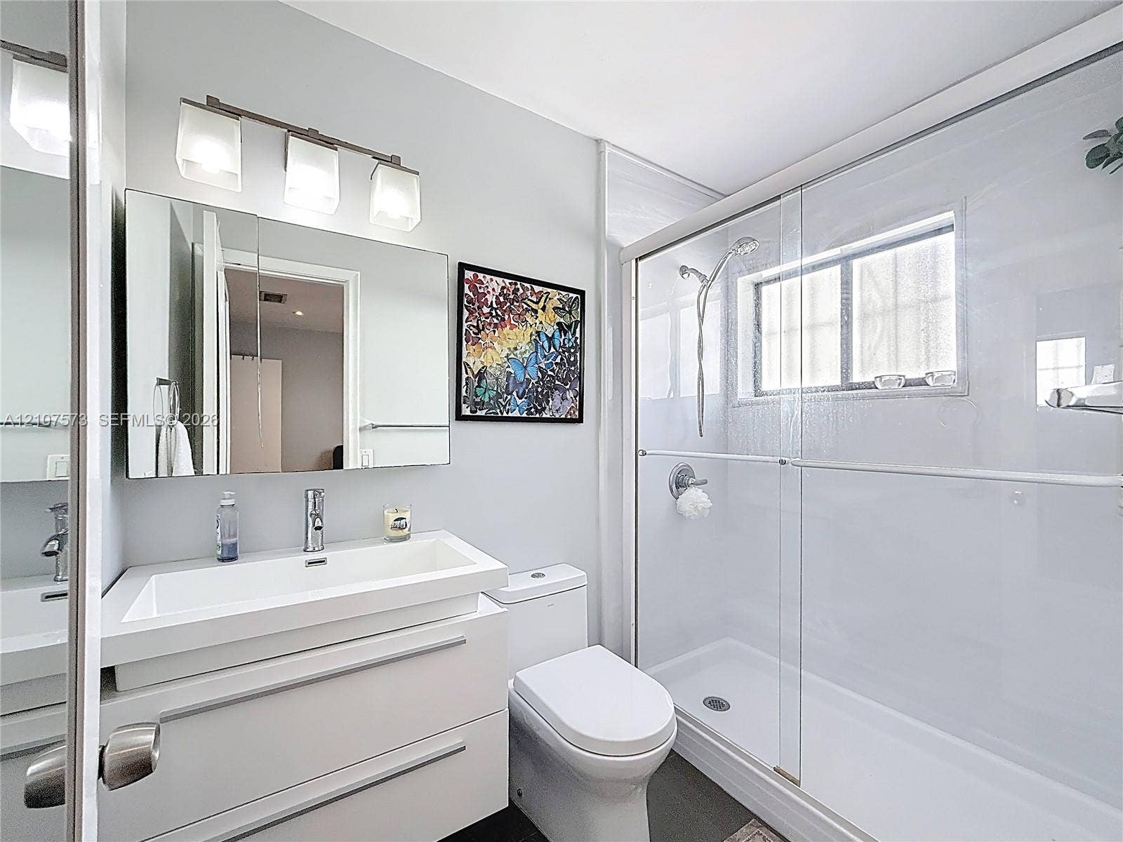 1291 SW 124th Court, #19-B, Miami, FL 33184 Modern floating vanity with a rectangular sink, three-light wall fixture, glass-enclosed shower with a handheld showerhead, and a medicine cabinet mirror