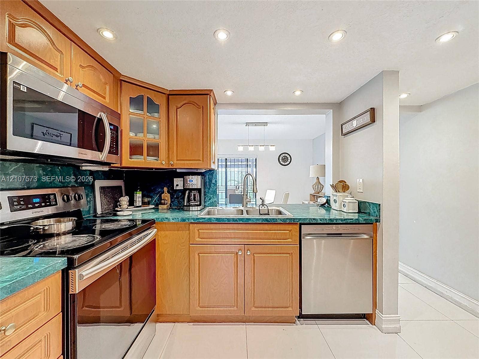 1291 SW 124th Court, #19-B, Miami, FL 33184 Kitchen featuring wood cabinetry with glass-front detailing, stainless steel microwave and dishwasher, solid-surface countertops, and recessed ceiling lighting