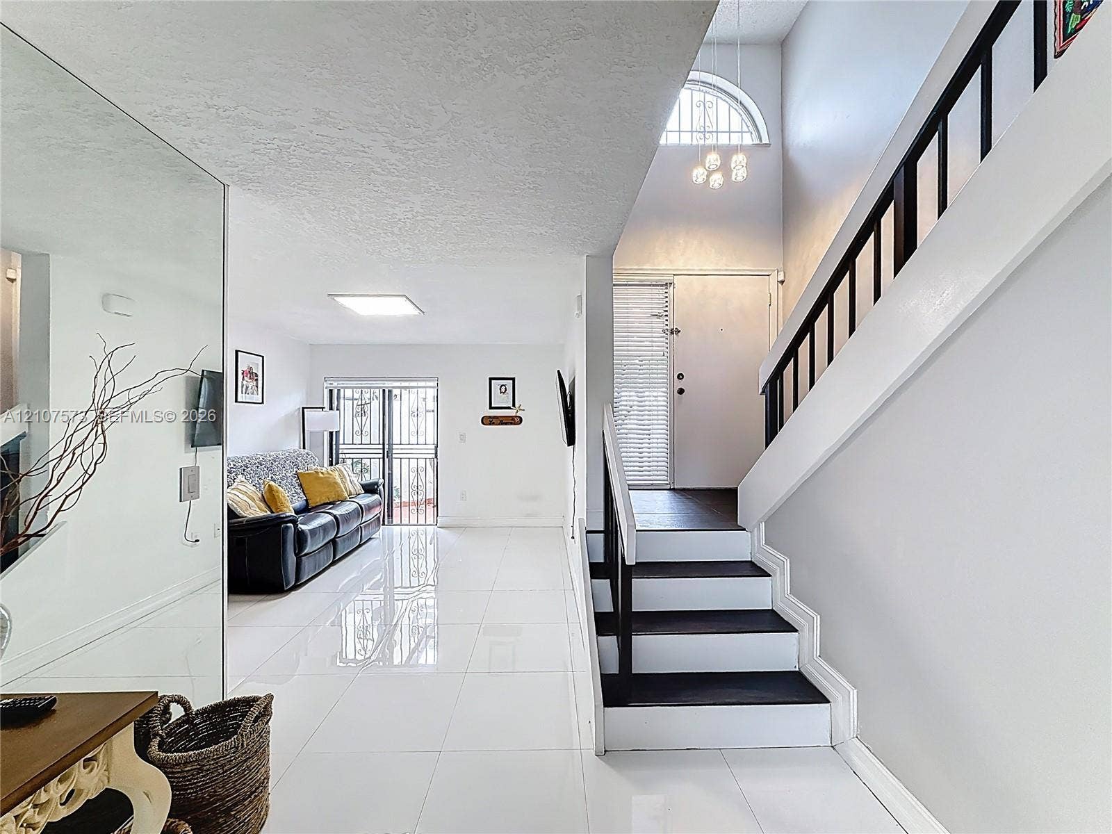 1291 SW 124th Court, #19-B, Miami, FL 33184 Entryway featuring high-gloss tile flooring, a mirrored wall accent, and a staircase with contrasting white risers and dark-toned treads