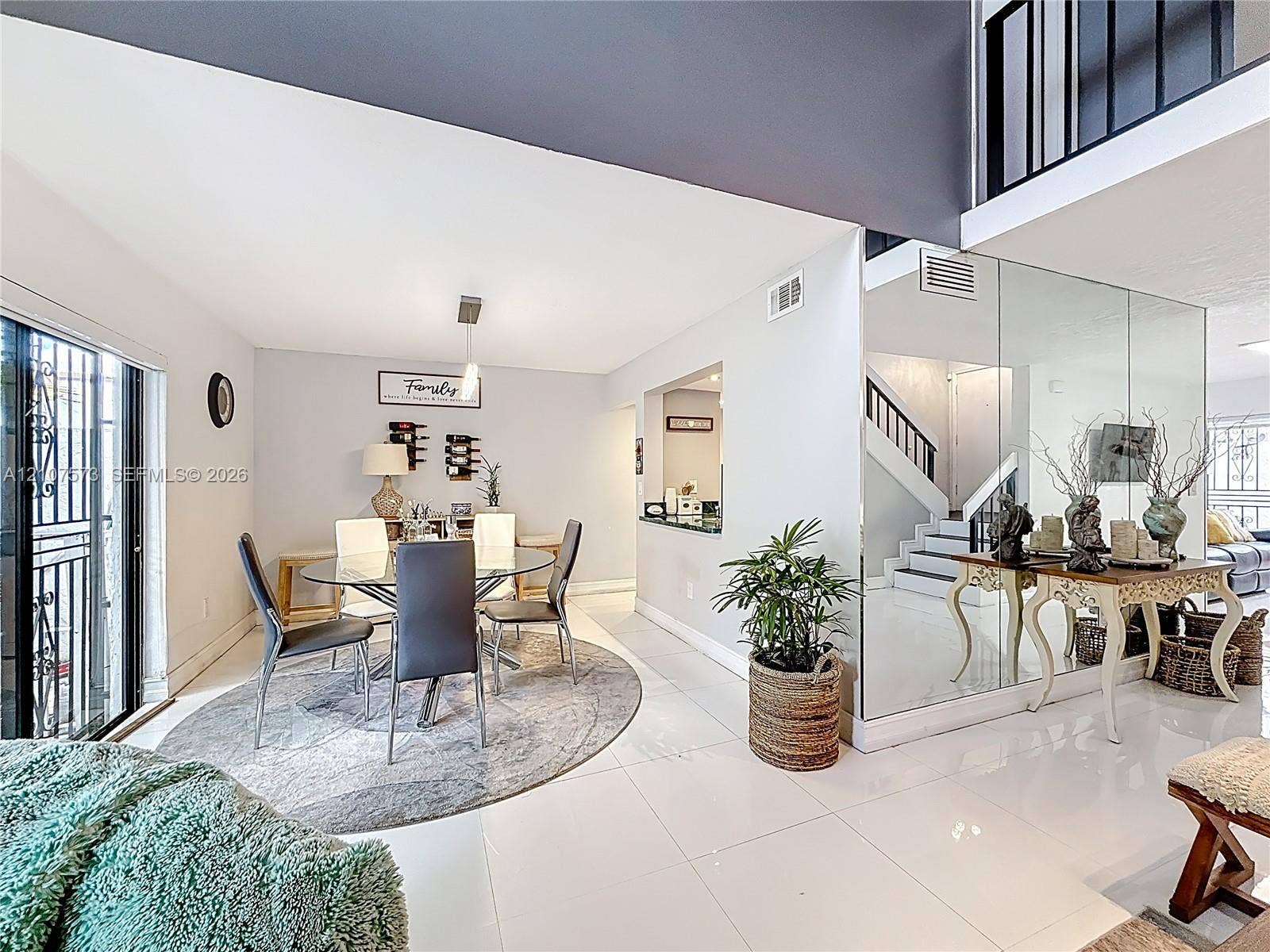 1291 SW 124th Court, #19-B, Miami, FL 33184 Open-concept interior featuring large-format tile flooring, double-height ceilings, mirrored wall accents, and an integrated staircase with a black metal railing