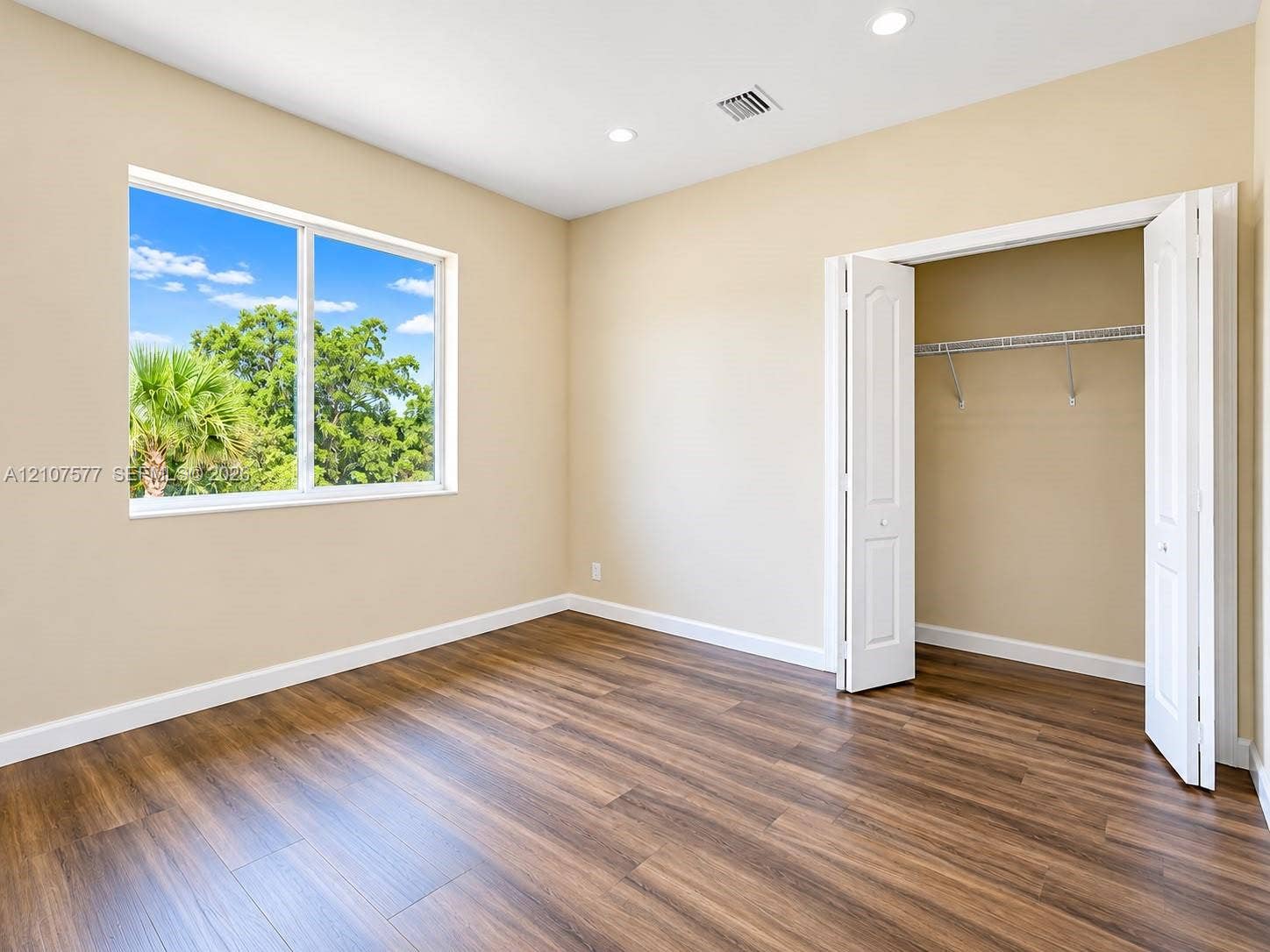 Room interior featuring wood-finish flooring, recessed lighting, a large picture window, and a closet with bifold doors