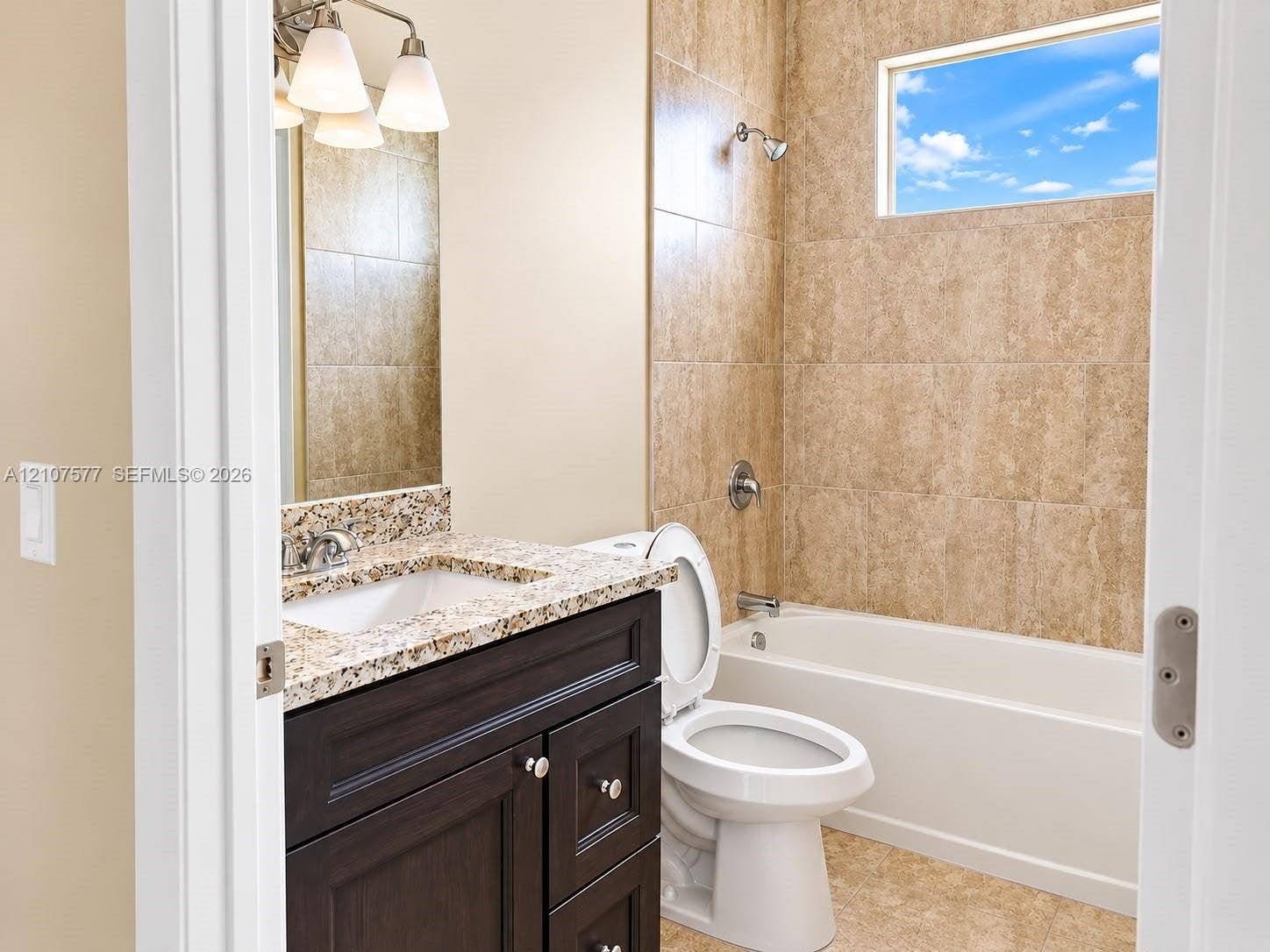 Bathroom featuring a dark wood-finish vanity, stone-pattern countertop with an integrated basin, tile-surround shower and bathtub combination, and transom window