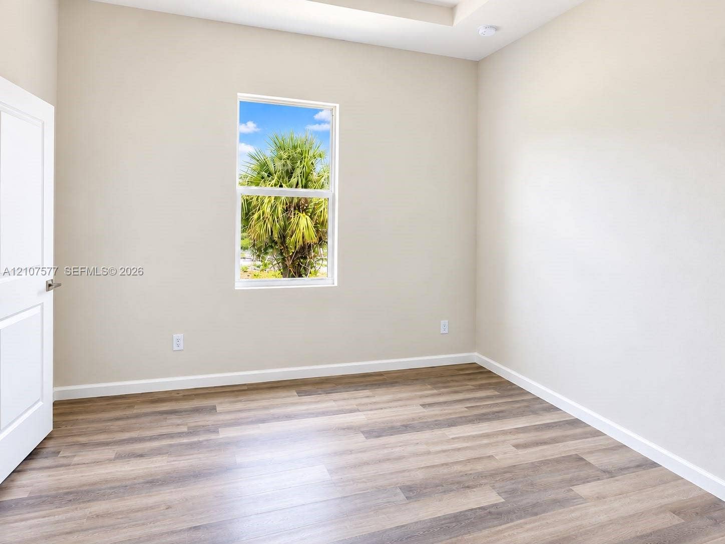 Neutral-toned interior room featuring wood-finish flooring, a recessed ceiling, a single-hung window, and a paneled door