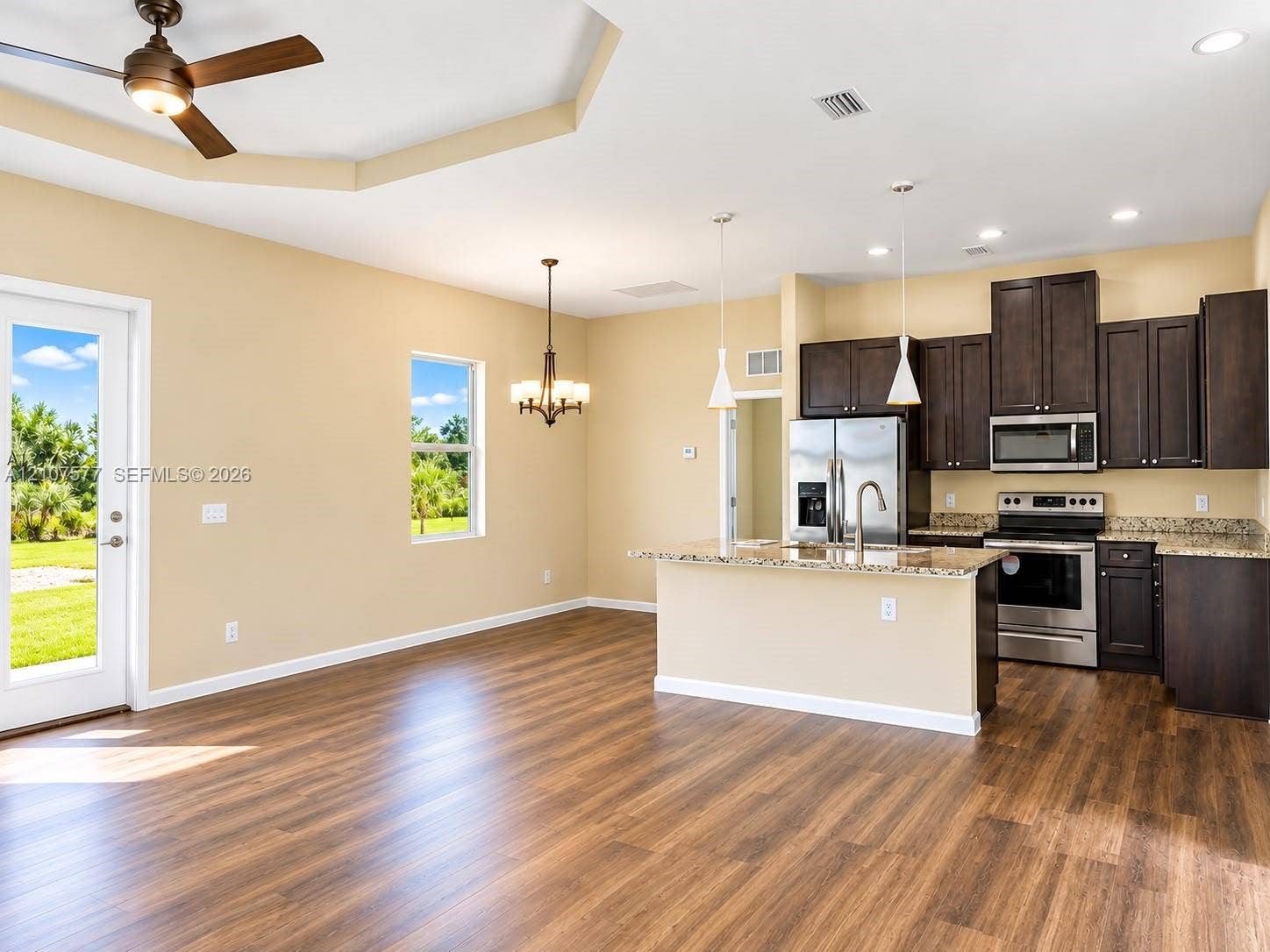 Kitchen featuring dark cabinetry, stone-finish countertops, stainless steel appliances, wood-finish flooring, and a trey ceiling