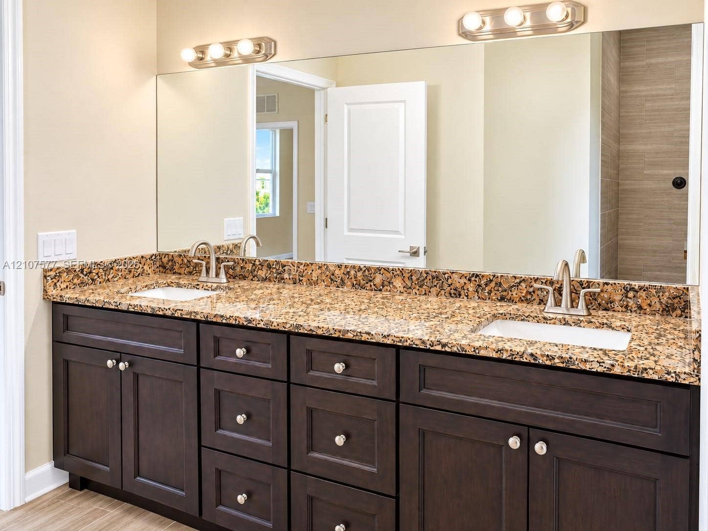 Dual-sink vanity with dark wood-finish cabinetry, stone countertop, undermount sinks, and wall-mounted vanity lighting