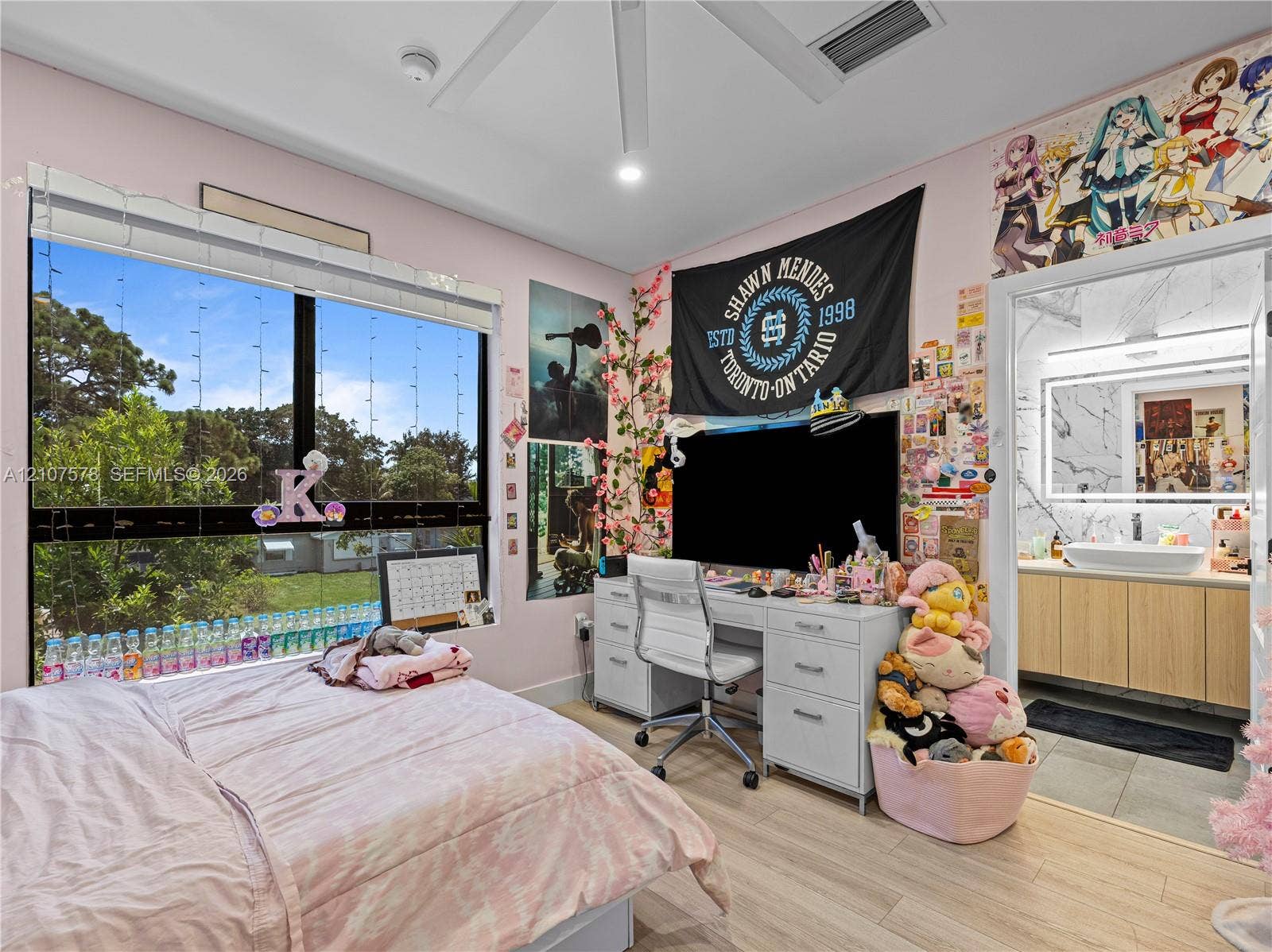 307 SW 10th Street, Fort Lauderdale, FL 33315 Large multi-pane window, wood-finish flooring, ceiling fan with integrated lighting, and en-suite bathroom featuring a light-wood vanity with a white vessel sink and backlit mirror