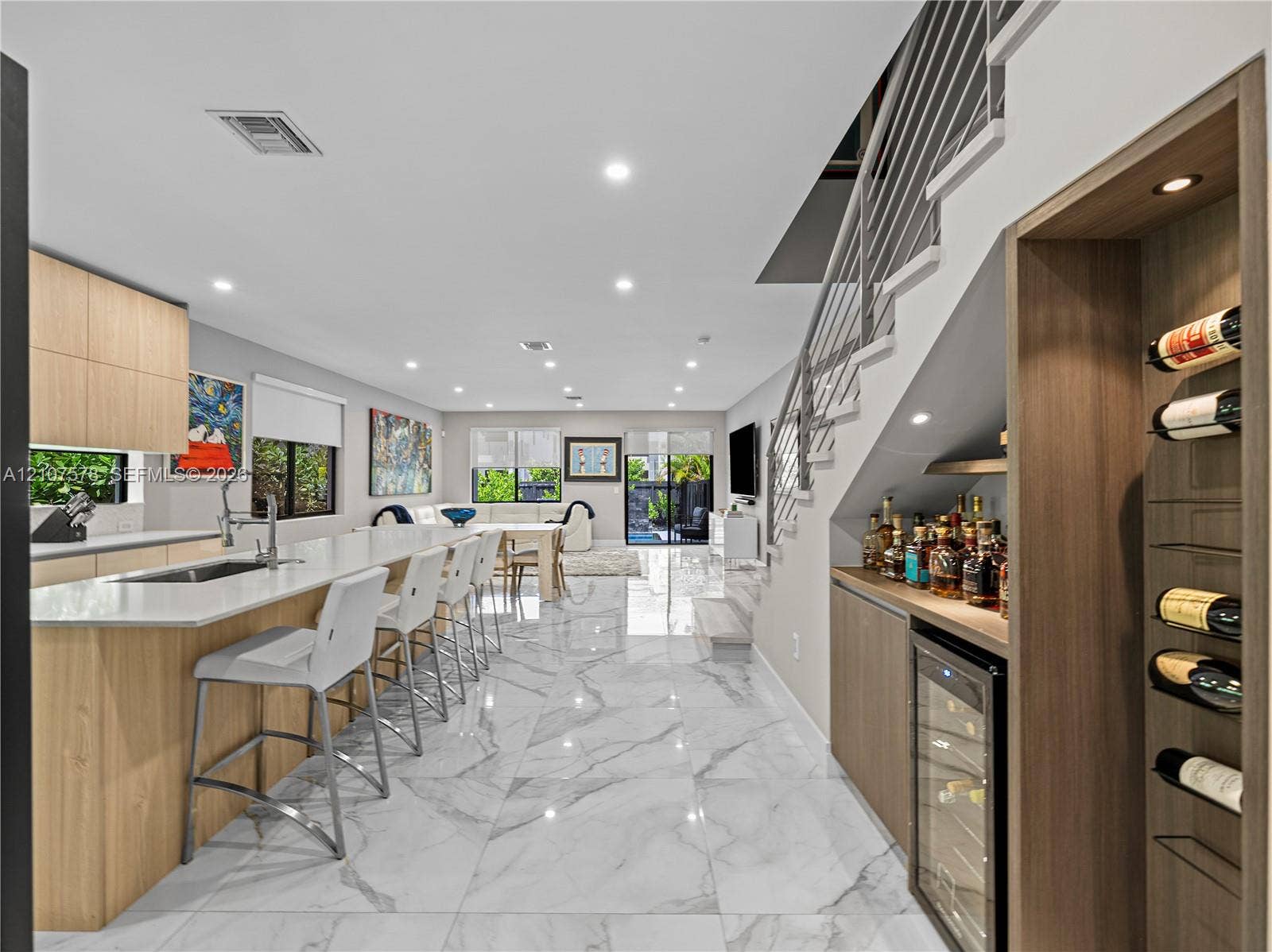 307 SW 10th Street, Fort Lauderdale, FL 33315 Open-concept kitchen featuring light wood-finish cabinetry, stone-surface countertops, large-format stone-finish flooring, a built-in wine cooler with integrated wine rack, and a staircase with metal railing