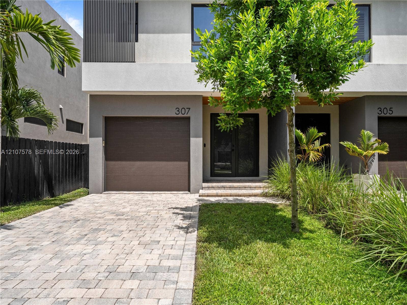 307 SW 10th Street, Fort Lauderdale, FL 33315 Modern two-story exterior featuring a paver driveway, an attached garage, glass-paneled entry doors, and professional landscaping
